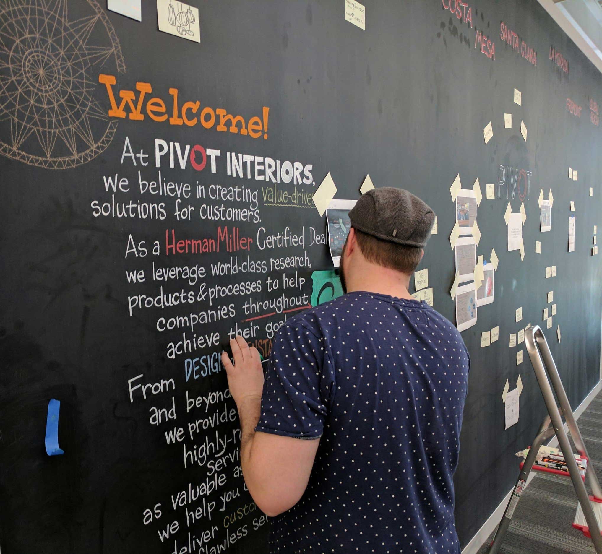 Peter Durand of Alphachimp is hand-lettereing the vision and mission statement of Pivot Interiors on the chalk wall.