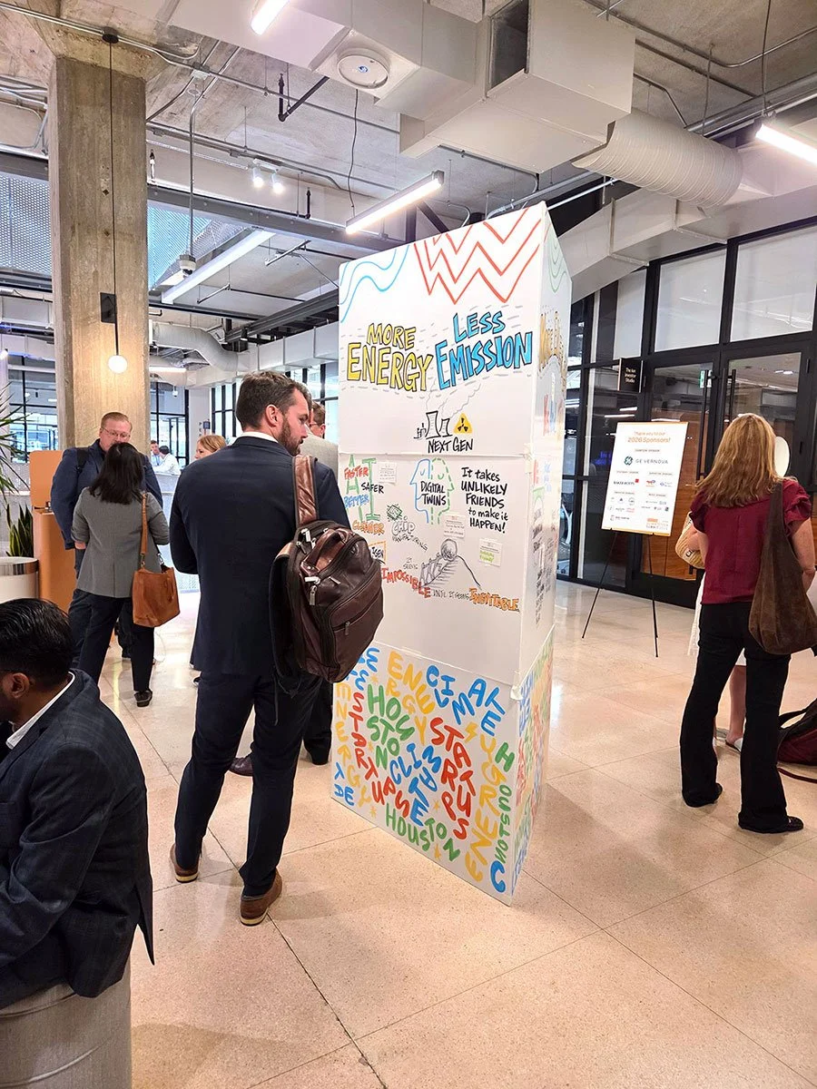 A participant in a blue suit with a leather backpack looks at graphic recording titled "More Energy, Less Emissions“ by Peter Durand, Alphachimp.