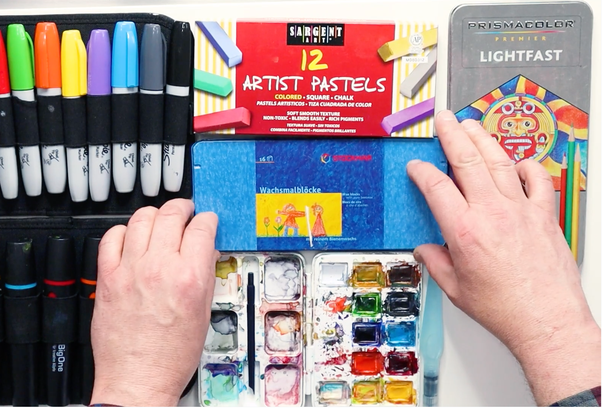 Various art supplies including Sharpie markers, Sargent Art pastels, watercolor paints, and Prismacolor pencils.