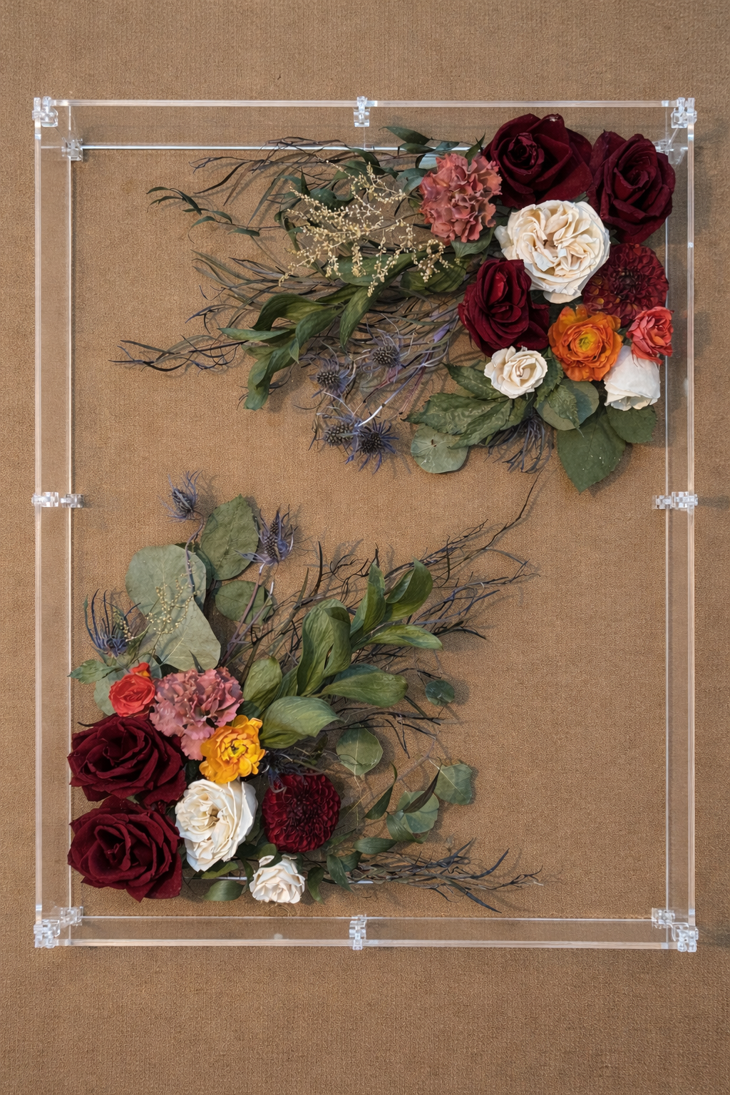 Floral art piece featuring red, white, pink, orange, and purple flowers with green leaves, arranged in a crescent shape on a transparent acrylic frame placed on a brown surface.