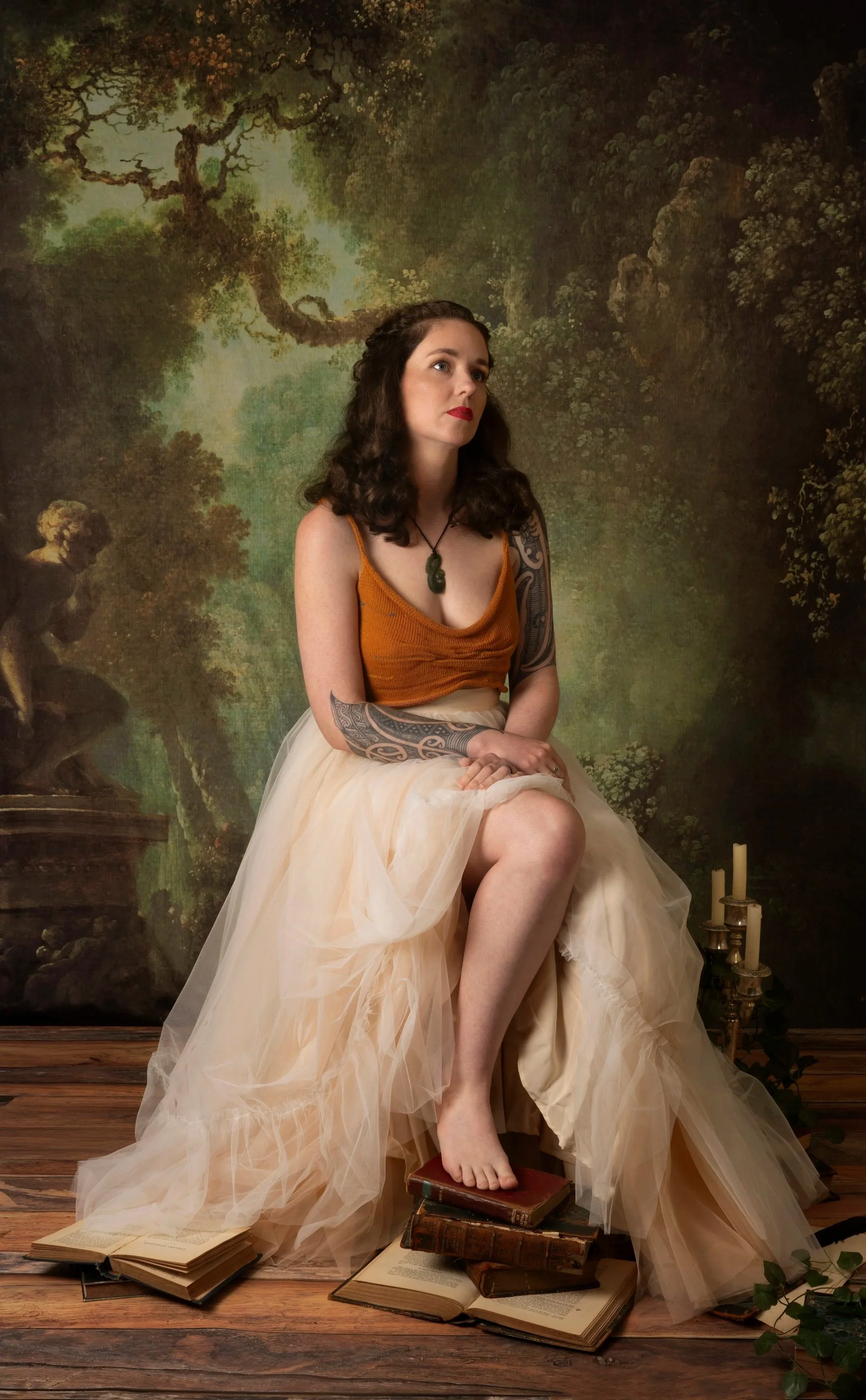 L. M. Woodward sits before a forest backdrop, one foot placed on a pile of books.