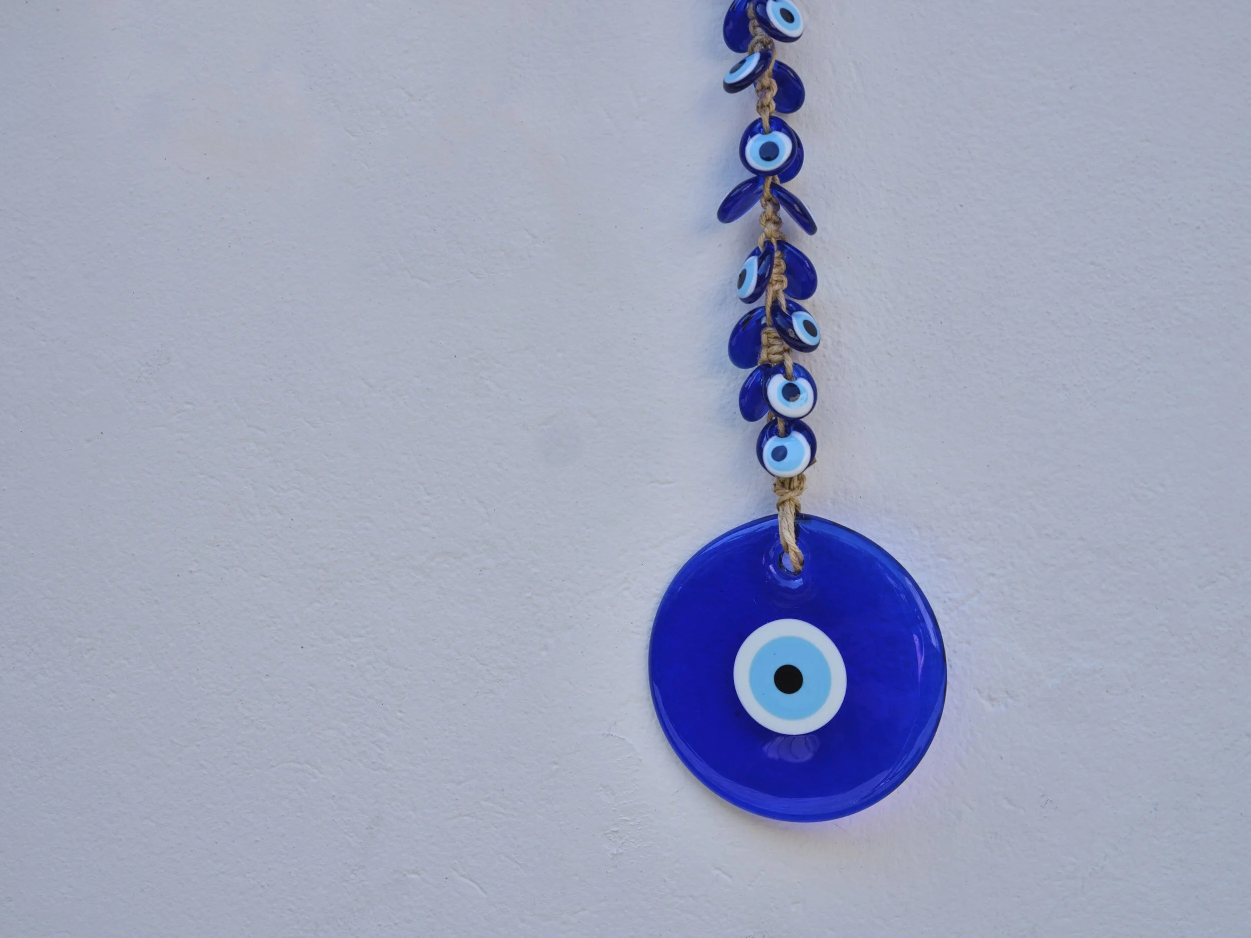 Blue glass Nazar boncugu amulet with multiple smaller Nazar charms hanging from a beige cord against a white background.