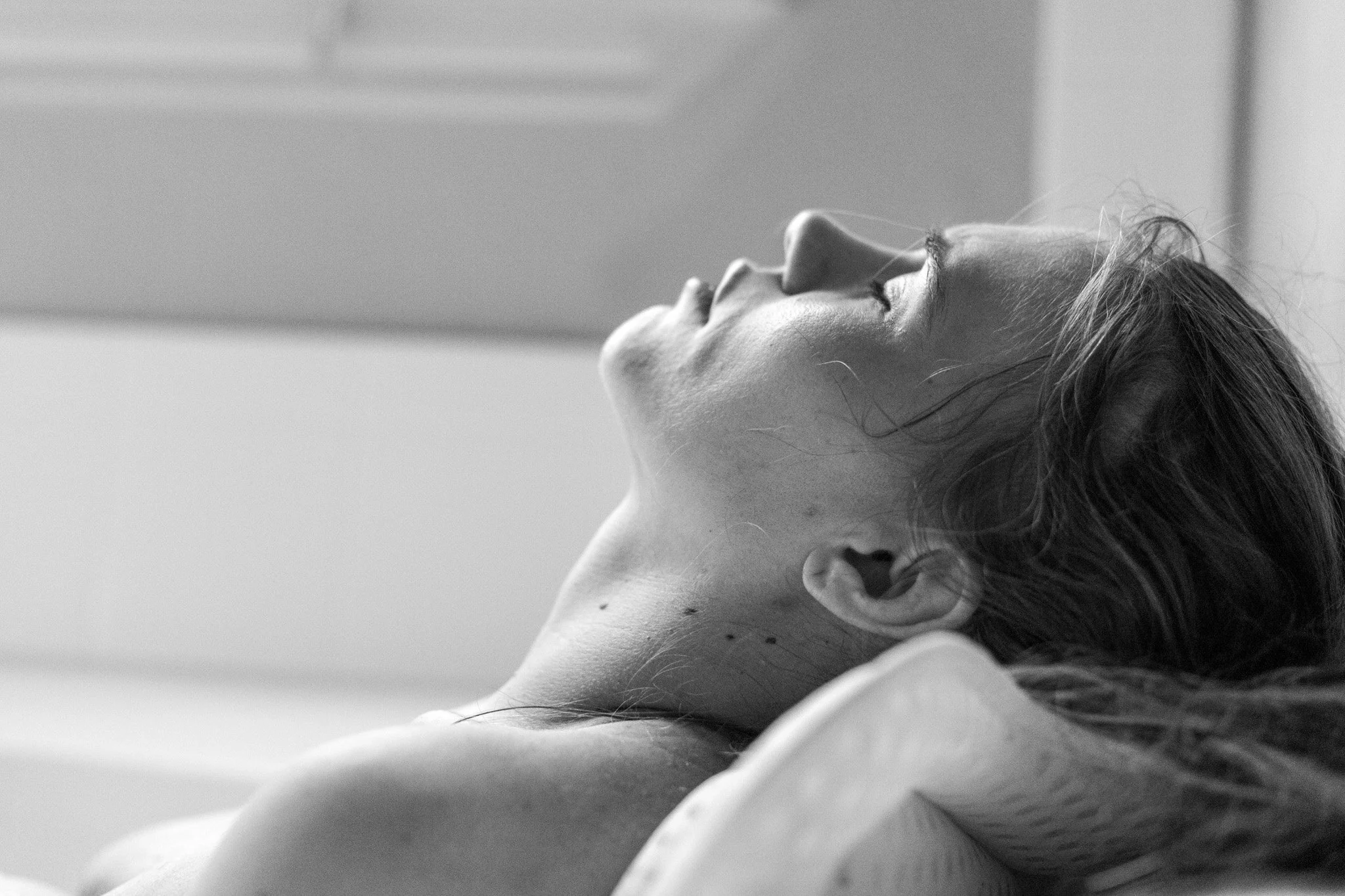 A woman lying in bed, resting with eyes closed, head tilted back, in black and white photograph.