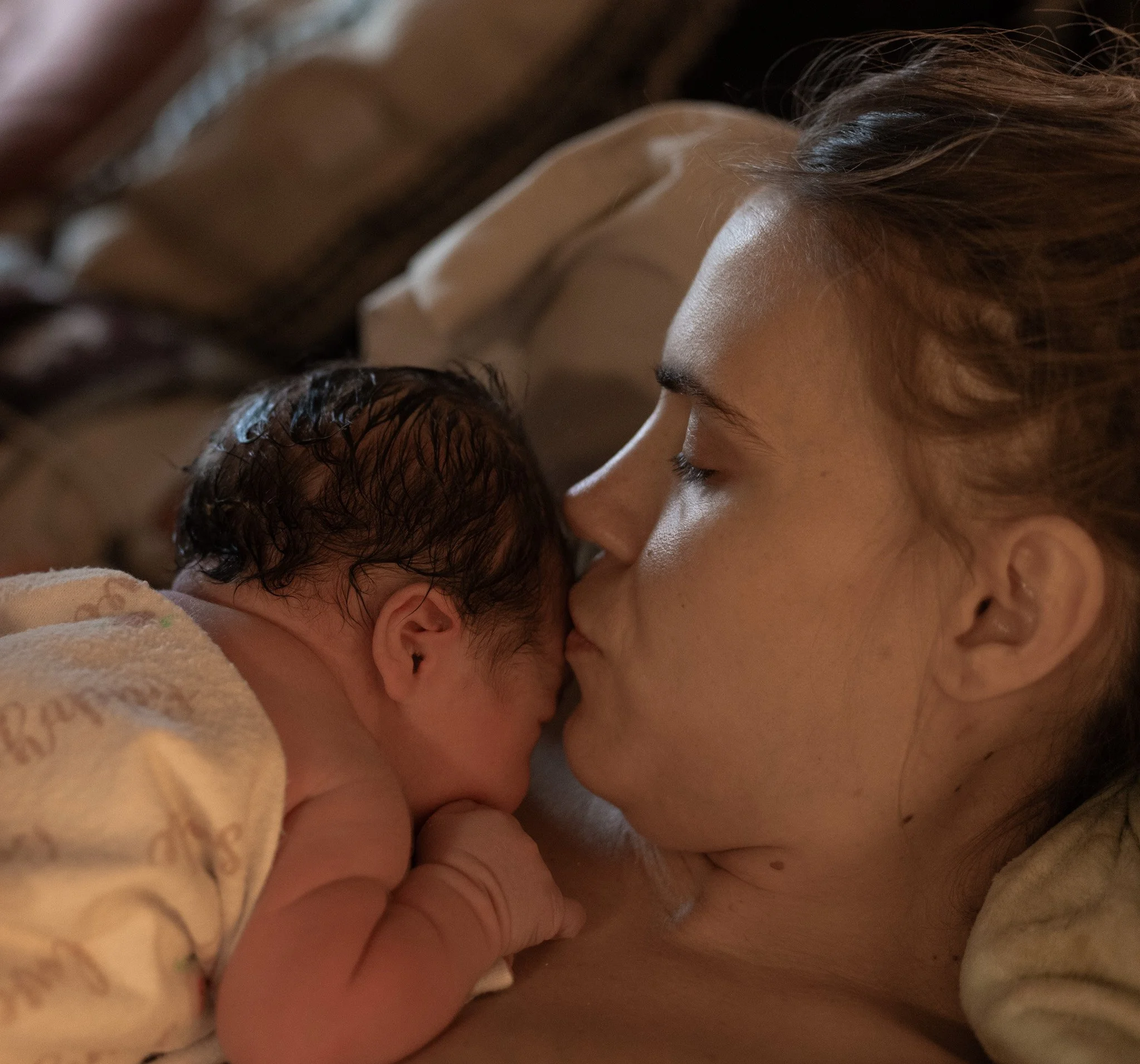 A newborn baby and a woman, likely the mother, share a close intimate moment, touching foreheads and eyes closed in a loving gesture.
