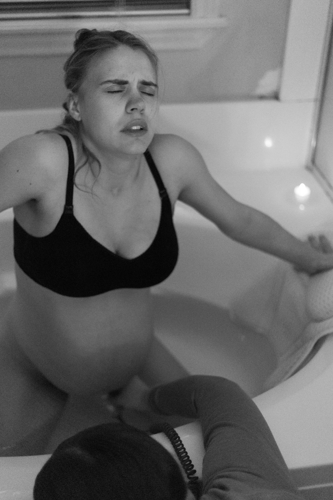 A pregnant woman with closed eyes and a distressed expression in a bathtub, with her head tilted back and one arm resting on the tub's edge.