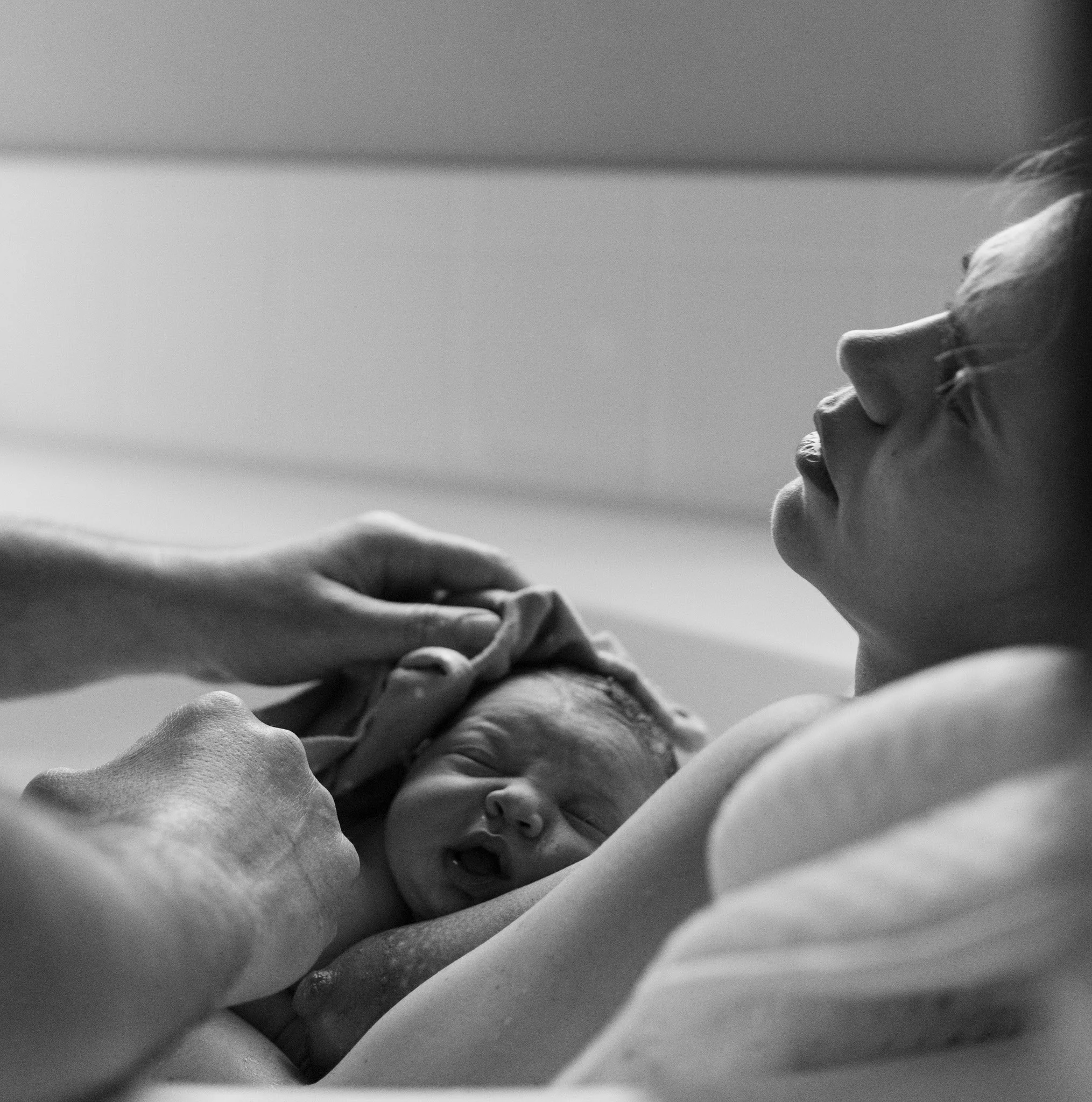 Black and white photo of a newborn baby being cradled by a woman; someone is gently touching the baby's head.