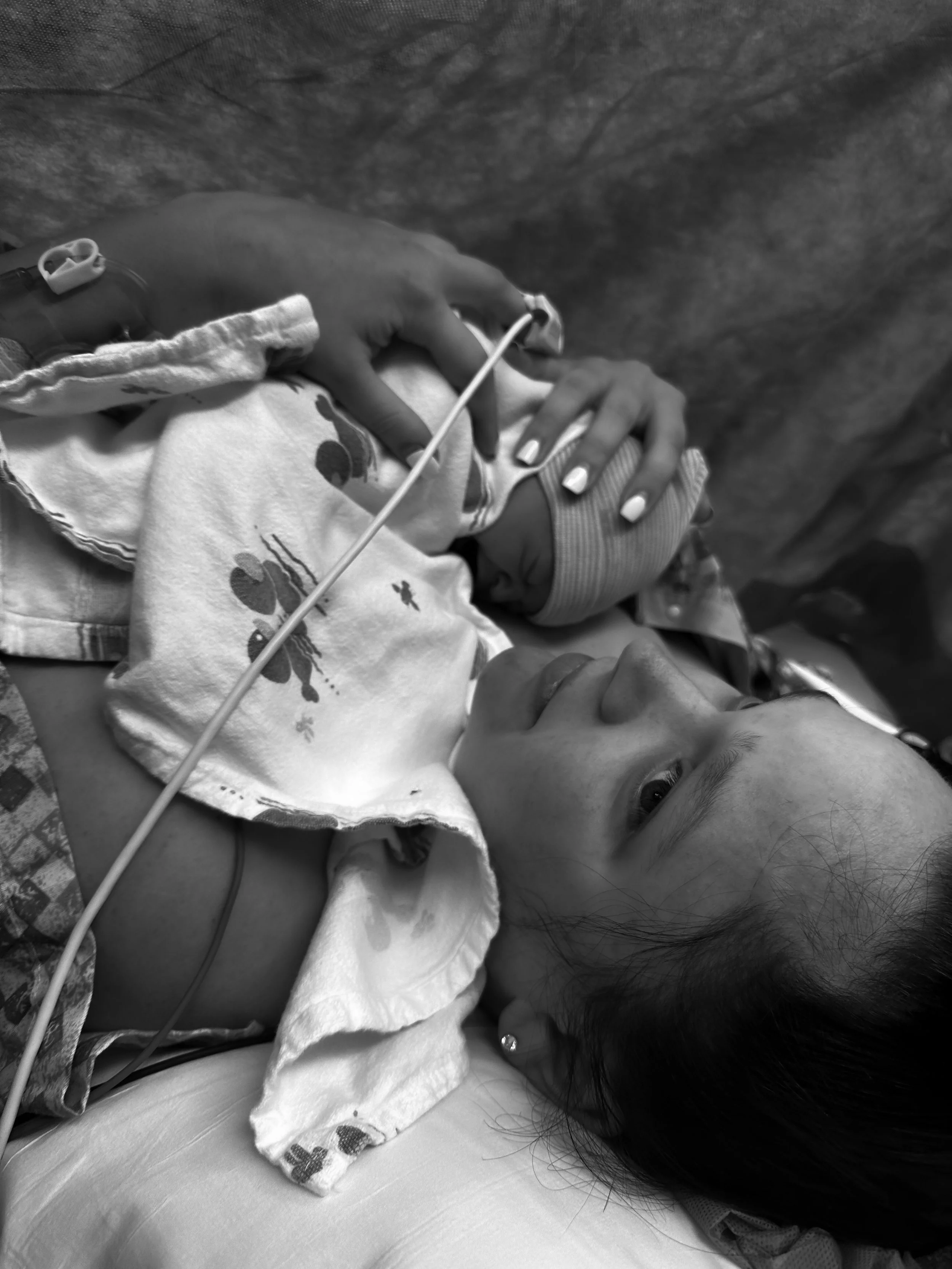 A young girl lying down in a hospital bed, wearing a striped cap, with an oxygen tube near her nose. A caregiver's hand gently holds her head, showing concern and care.