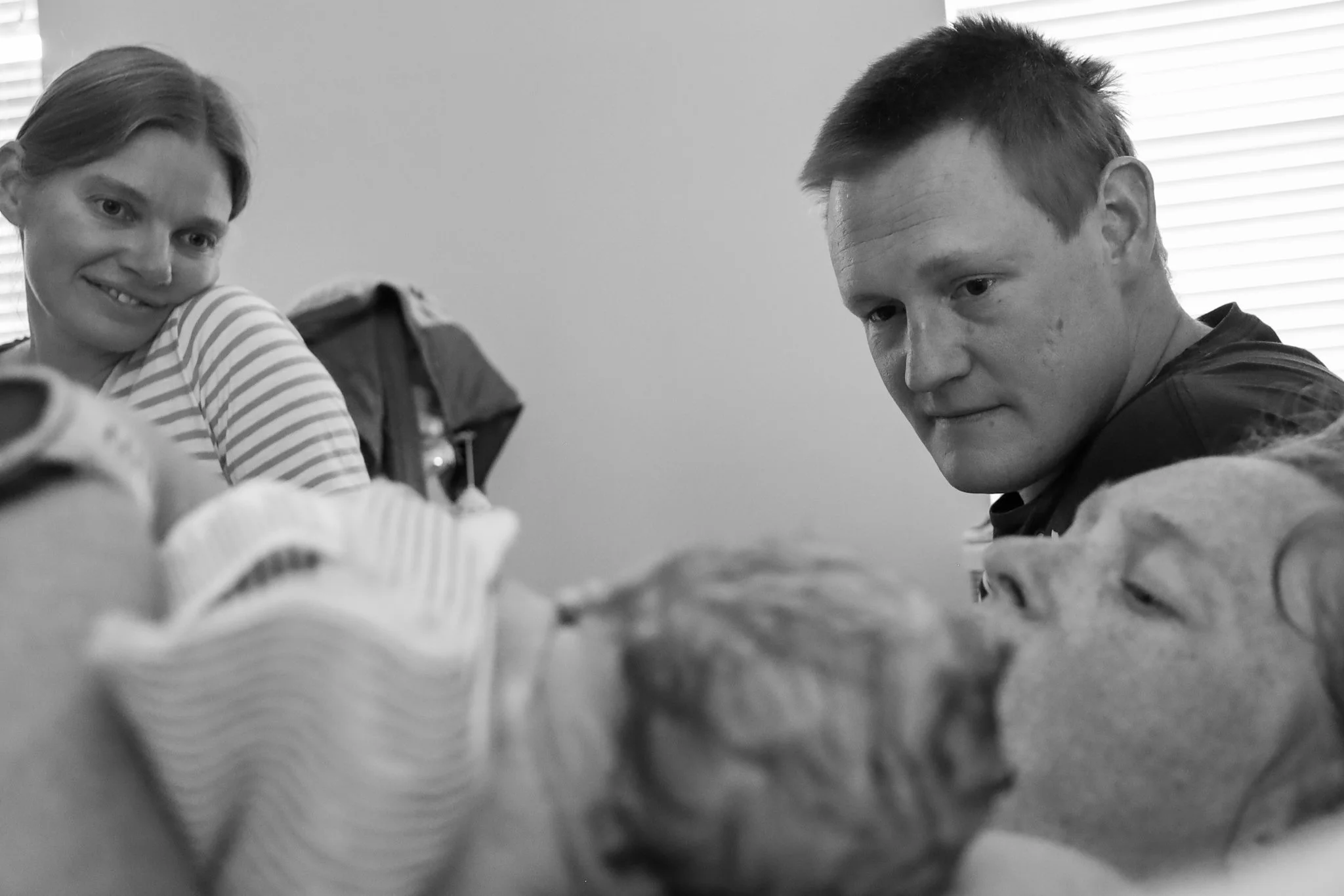 A doula, woman and a man look at a newborn baby in a hospital setting.
