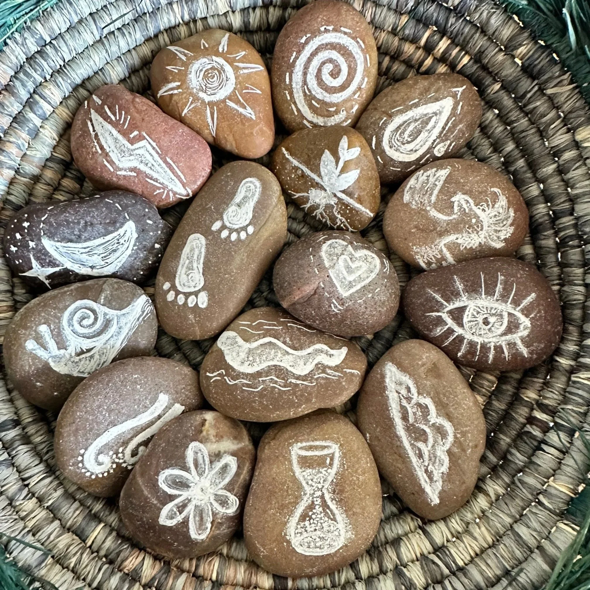 A collection of hand painted rocks with nature motifs and symbols in a woven basket.
