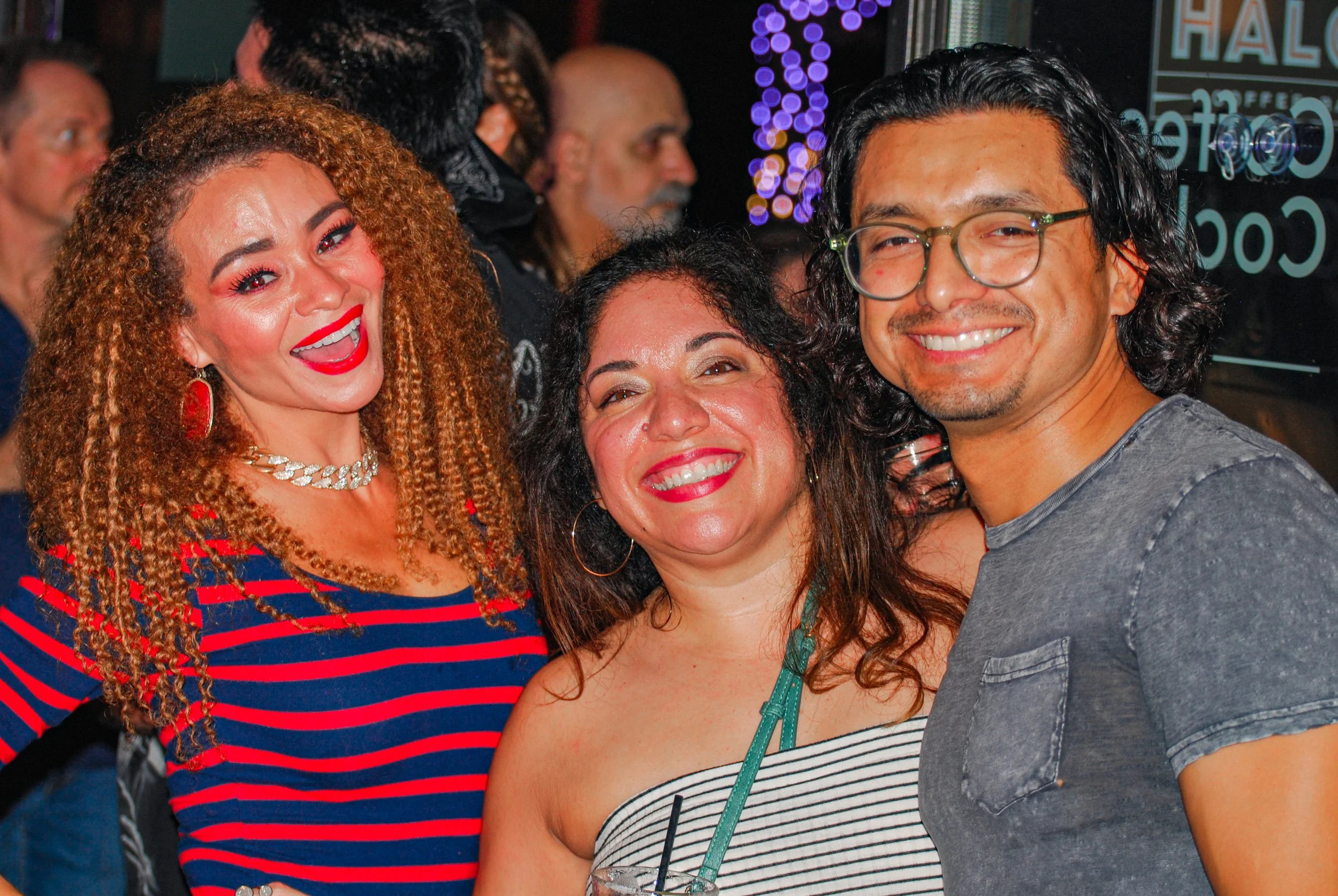 Three smiling friends at a nighttime social event, two women and one man, posing closely together. Austin, TX