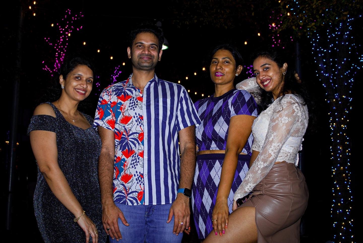 Group of five people standing outdoors at night, decorated with colorful string lights in the background. Austin, TX
