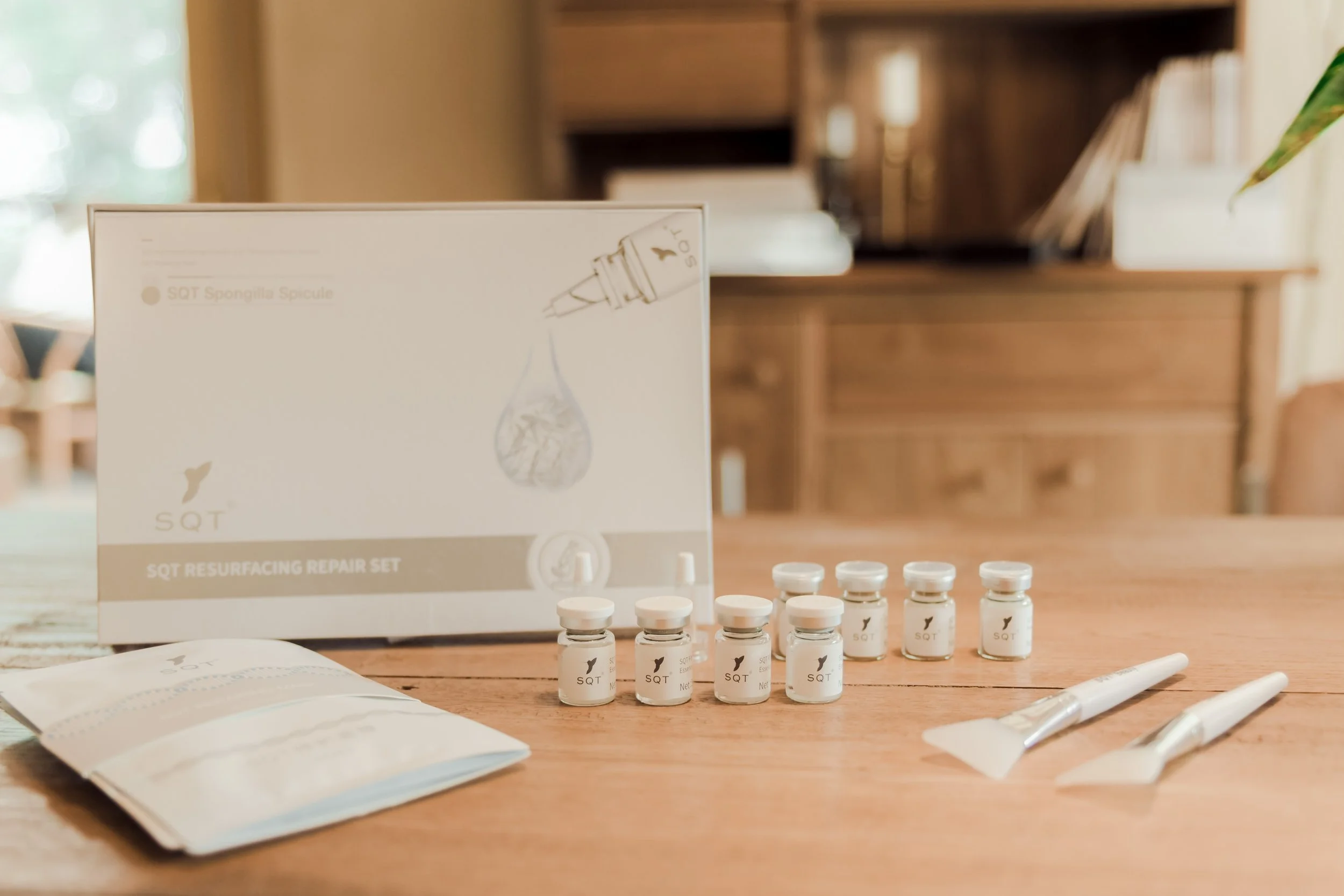SQT Resurfacing Repair Set with small vials, two spatulas, and a booklet on a wooden table in a room with wooden furniture.