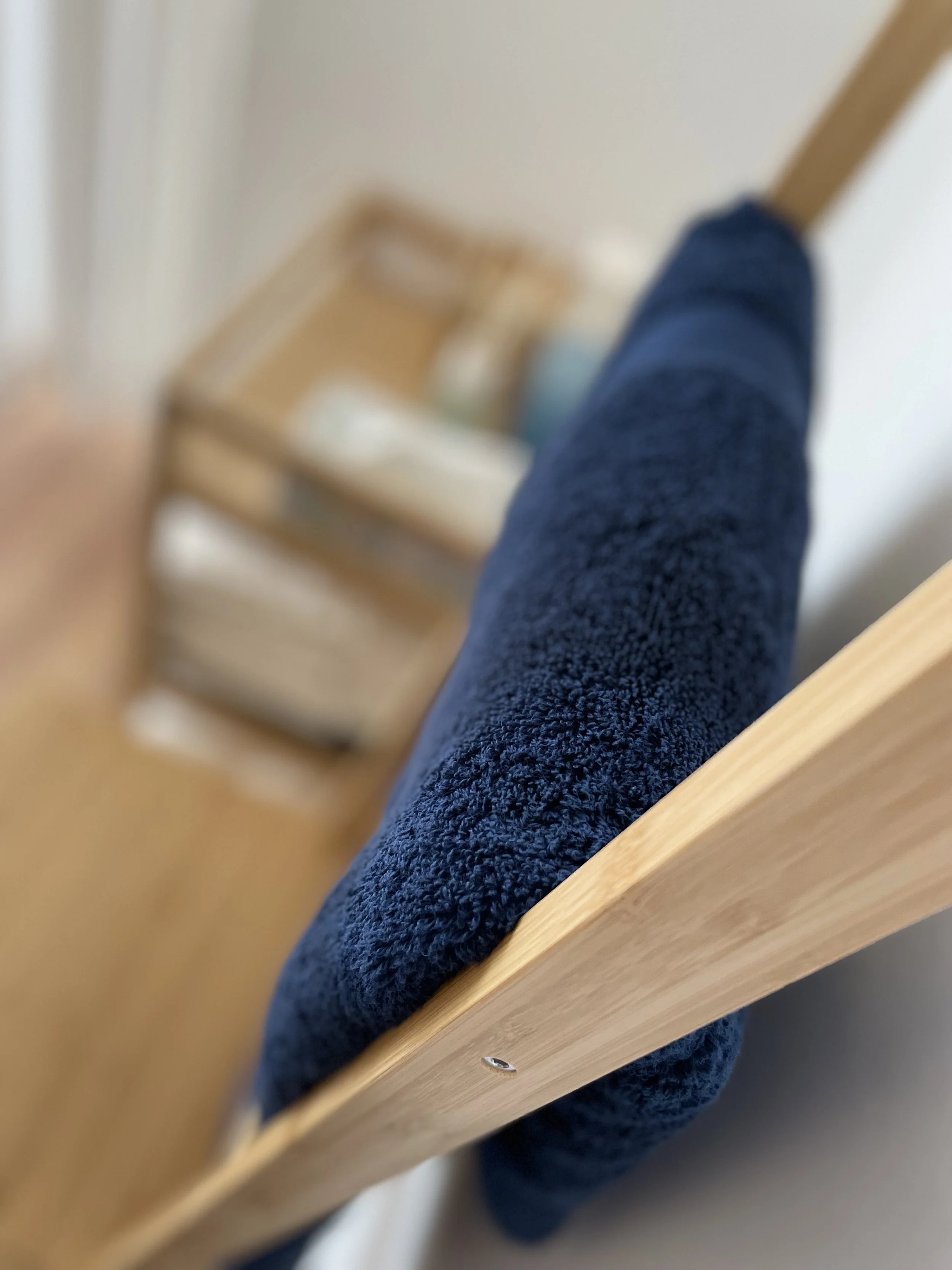 Close-up of a blue towel hanging over a wooden railing, with a blurred background of a wooden chair and some household items.