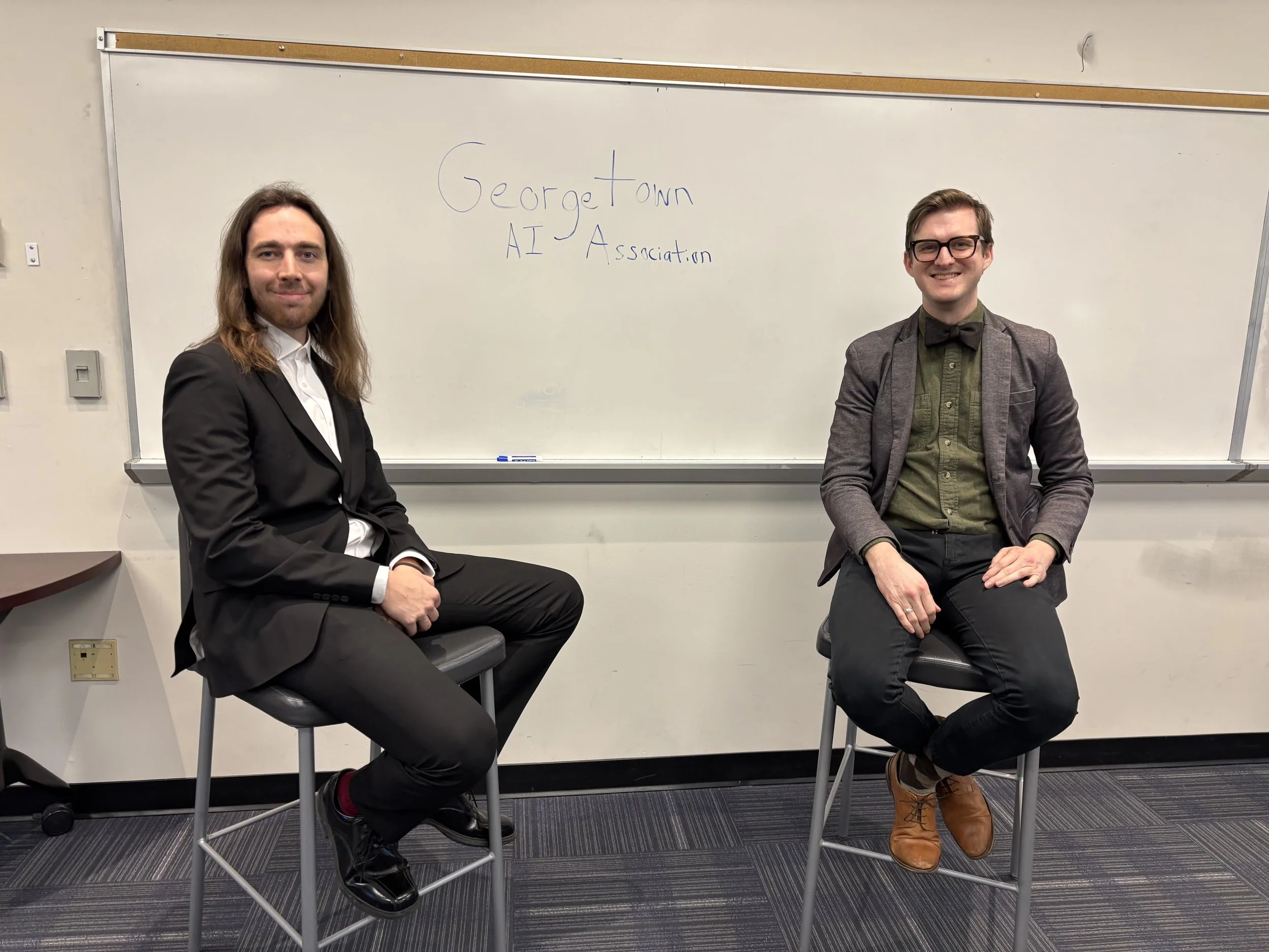 Panelists seated at a panel in a classroom or lecture hall, with a large screen displaying a welcome message and information about the Georgetown Responsible AI Network, logos of various organizations, QR codes, and a description of the event.