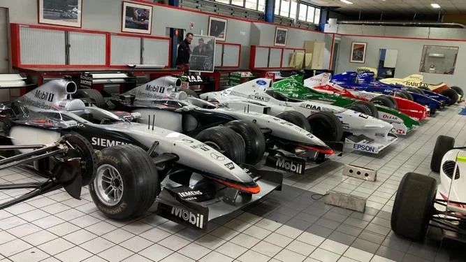Ventes de formules 1 dans un musée ou un centre d'exposition, avec plusieurs voitures de course alignées.