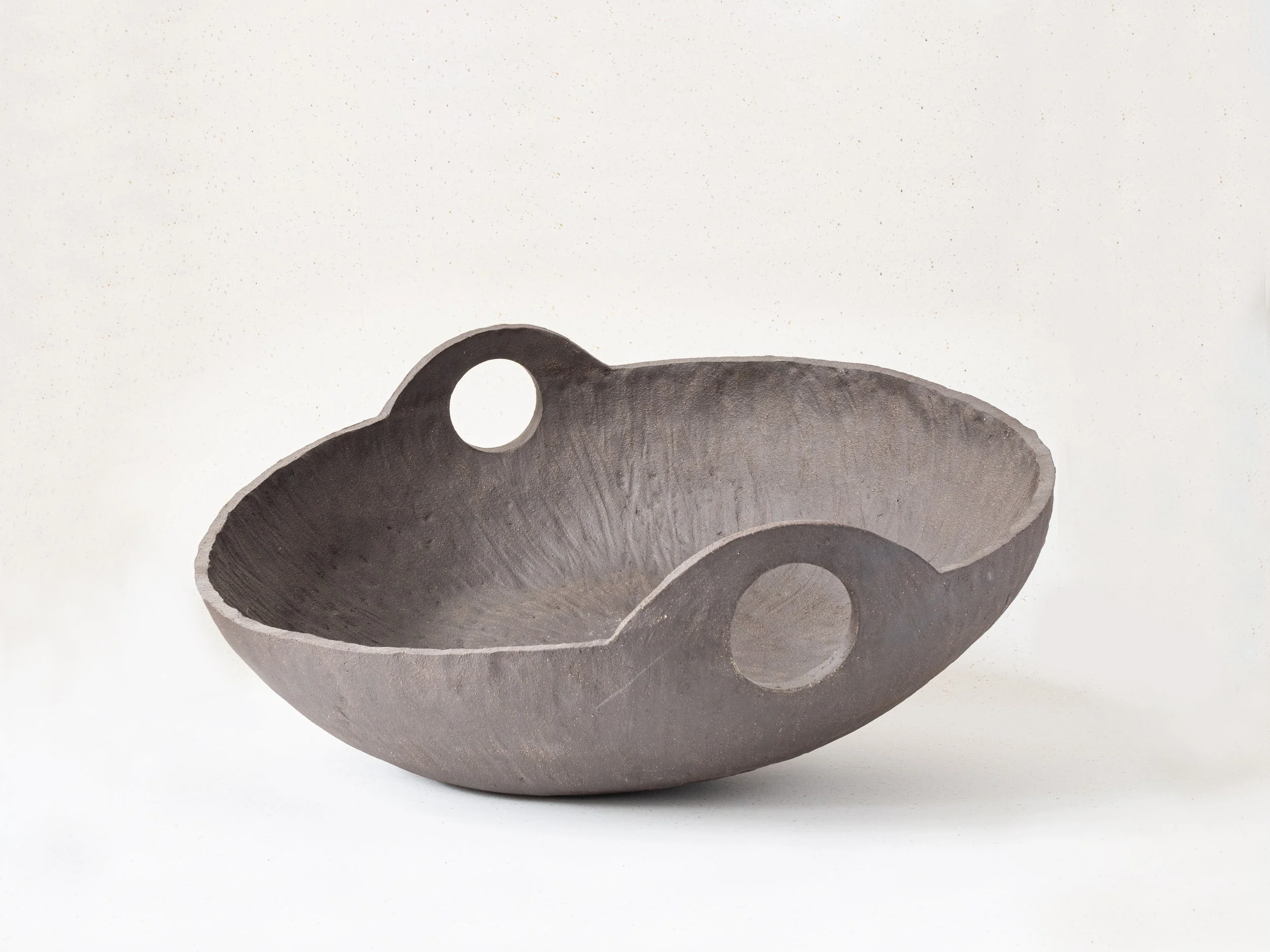 Black ceramic vessel with a round hole handle near the top, displayed against a plain background.