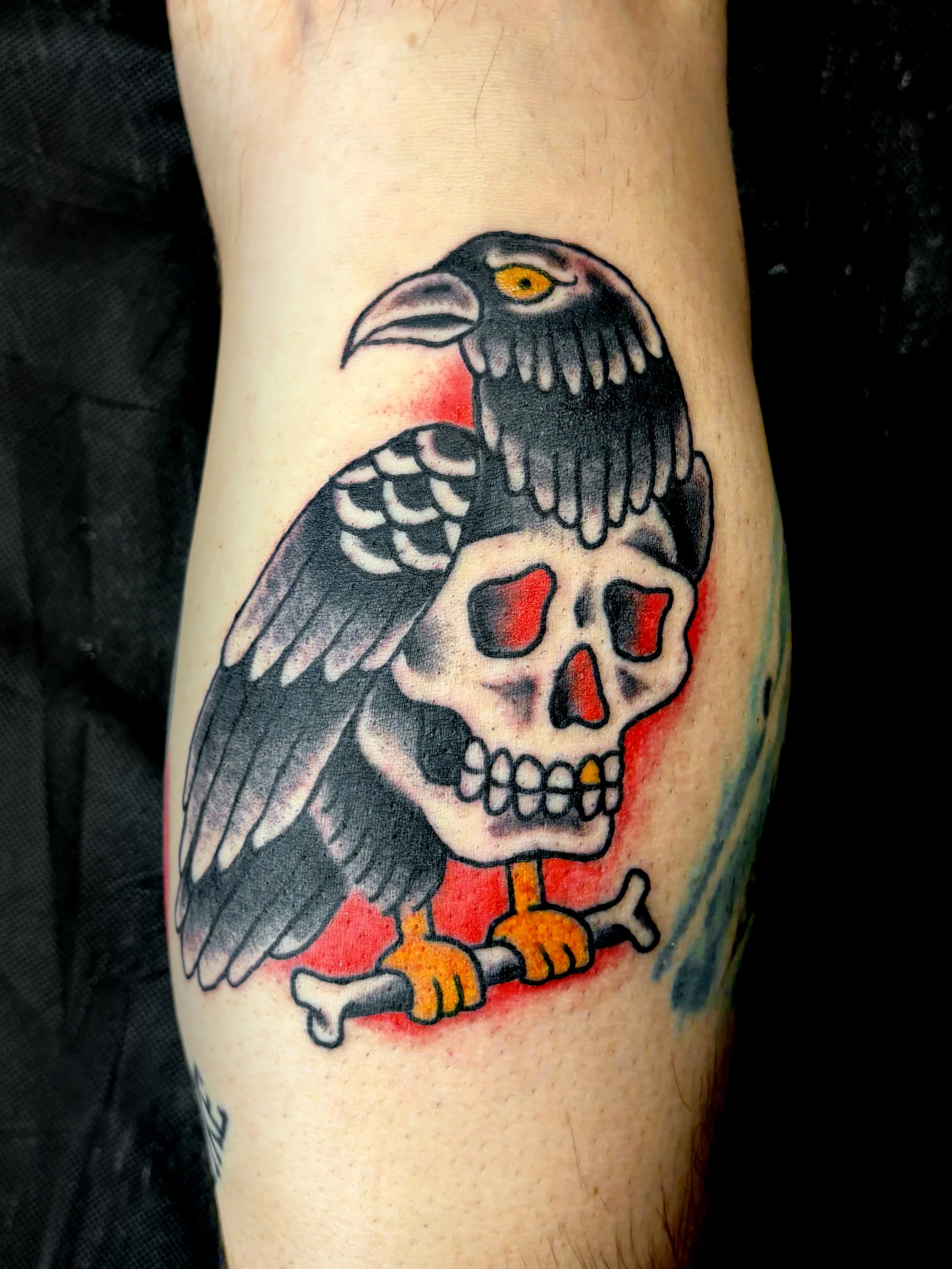 american traditional tattoo of a crow with a skull for a body in red, yellow and black 