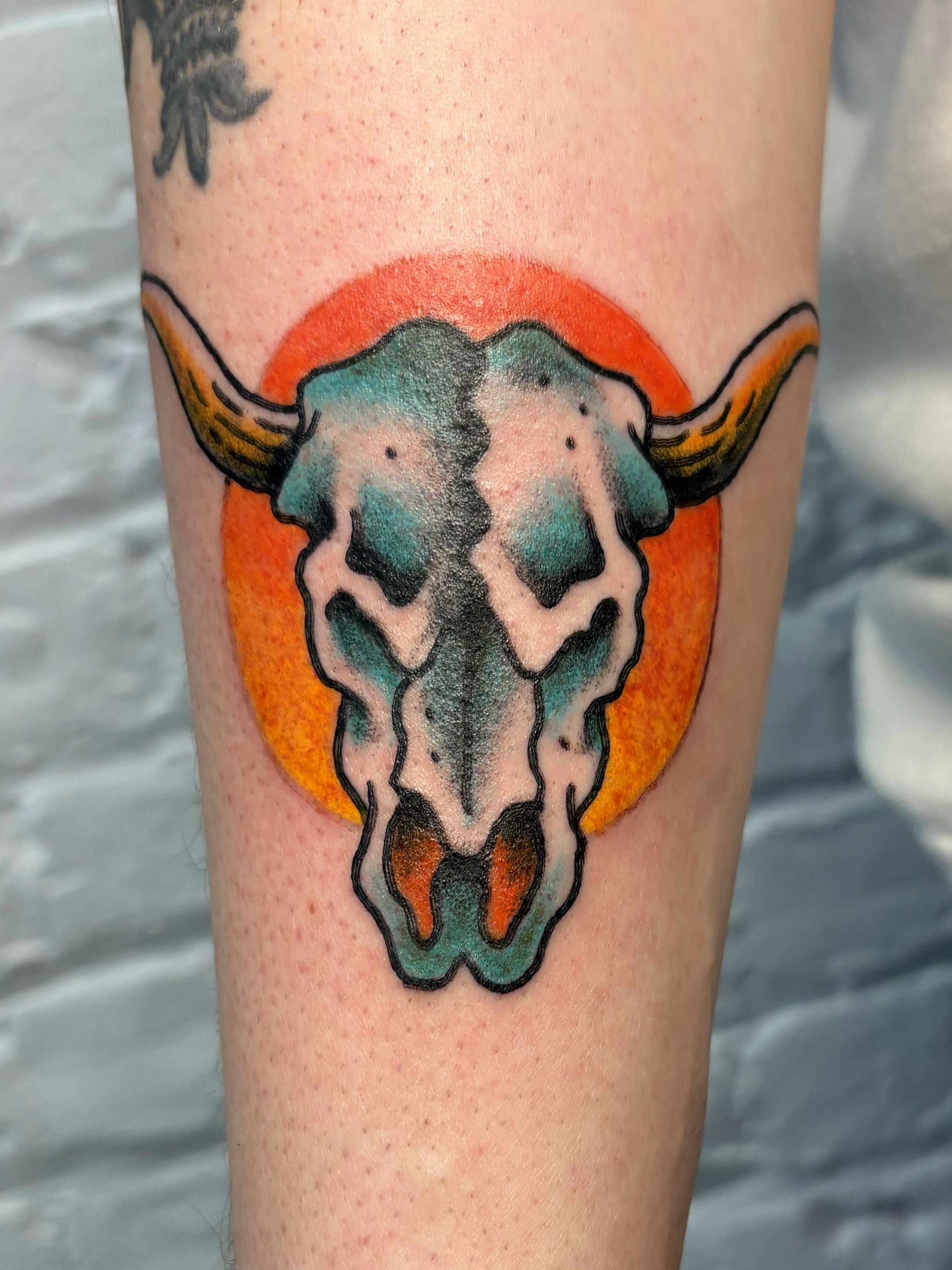 american traditional tattoo of a texas longhorn skull with a sunset behind the head. with pops of blue ad yellow and orange