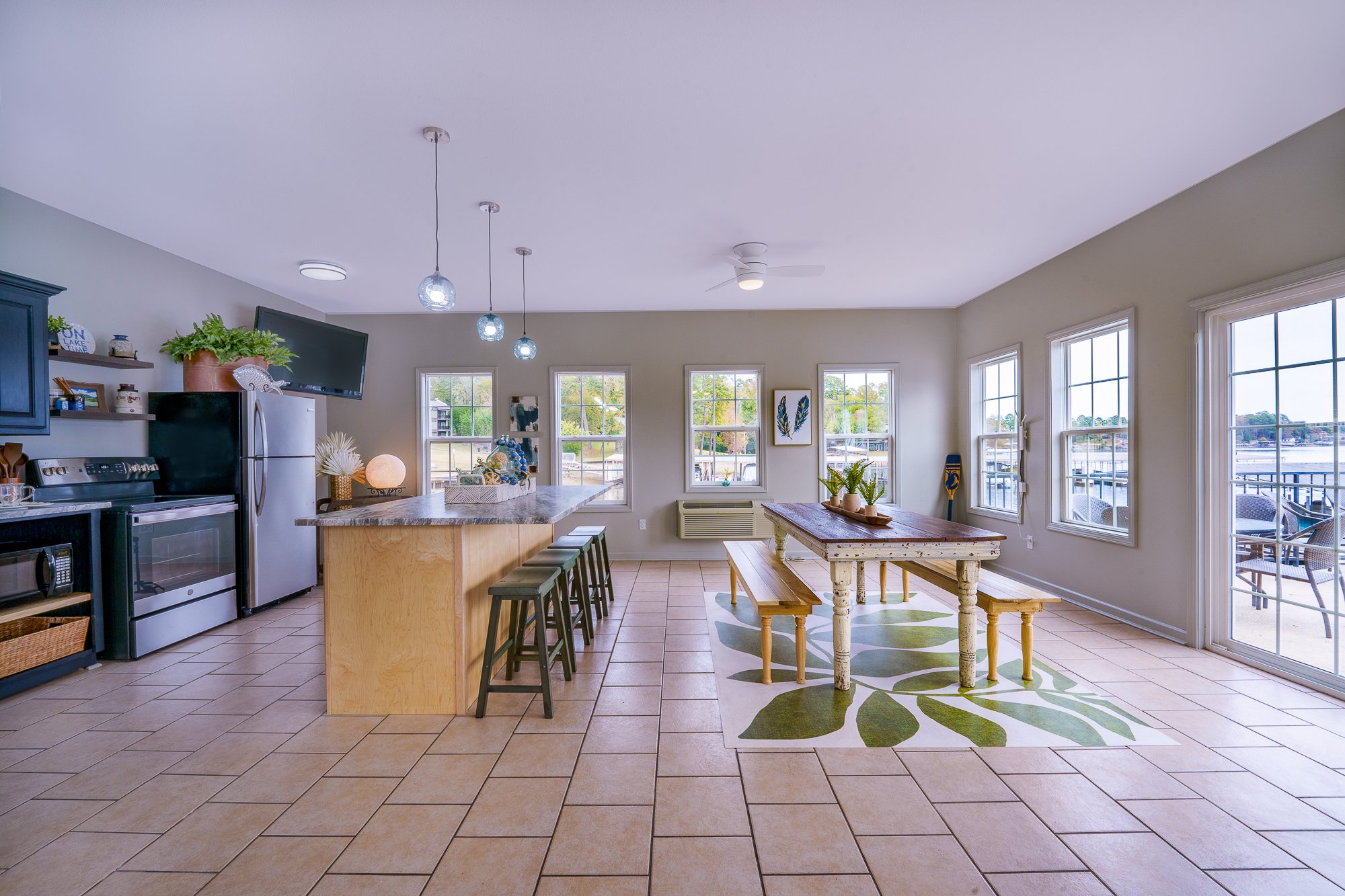 Modern kitchen with island, stools, and dining area with benches, overlooking a view through large windows.