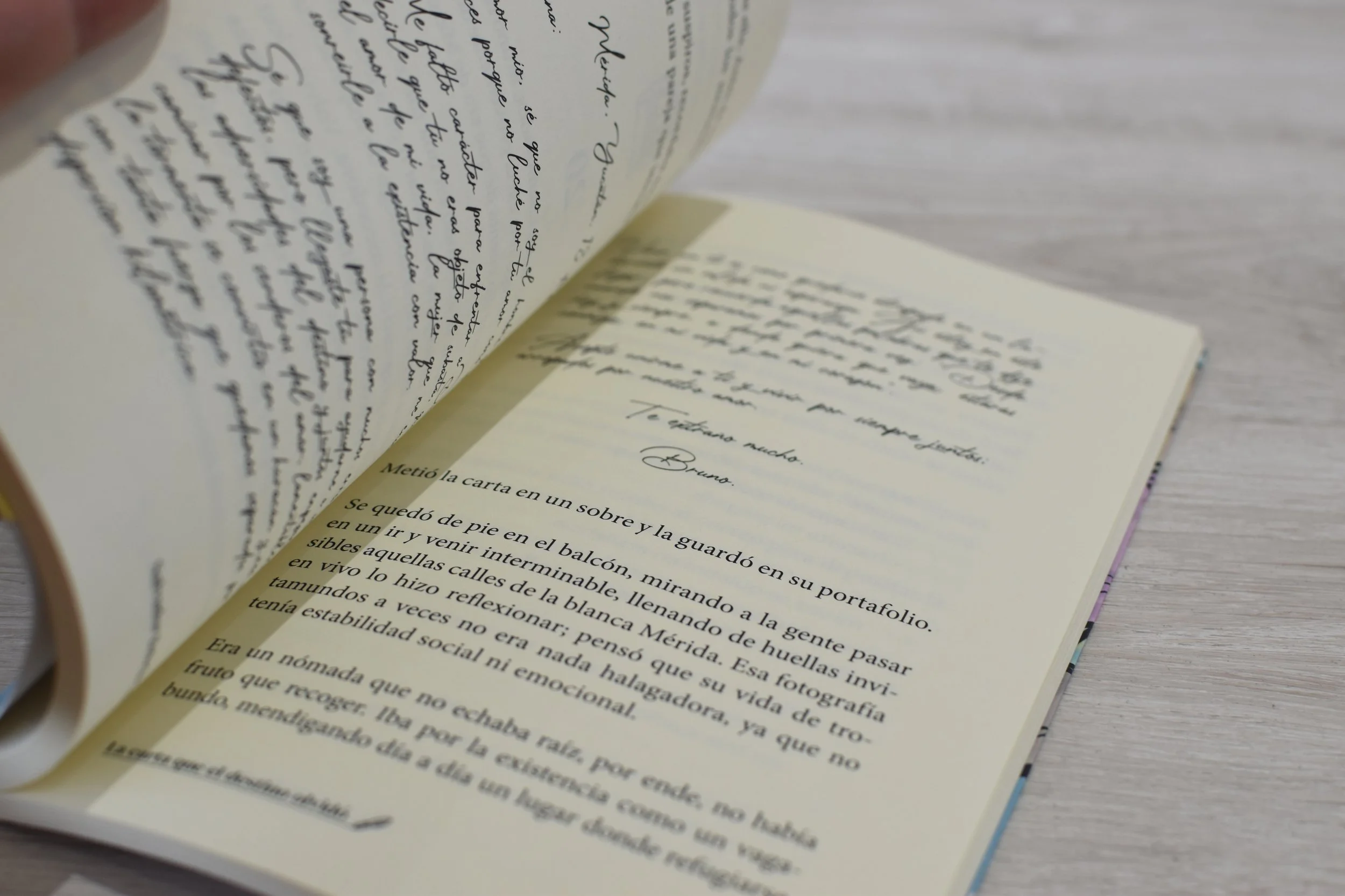 Página de un libro con texto en español, con letra manuscrita y en cursiva, sobre un fondo beige. La página está ligeramente doblada en la esquina superior izquierda y se encuentra sobre una superficie de madera clara.