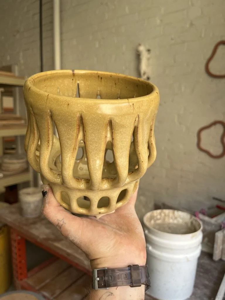 A yellow ceramic decorative vase with tentacle-like protrusions held in a person's hand in a pottery studio.