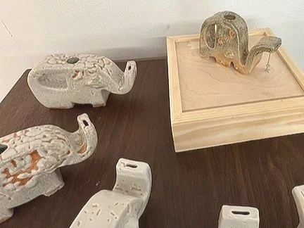Four ceramic elephant figurines on a table, with one elephant figurine inside a wooden tray.