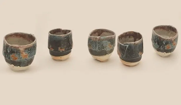 Five small ceramic cups with abstract blue and orange patterns, arranged in a row on a plain surface.