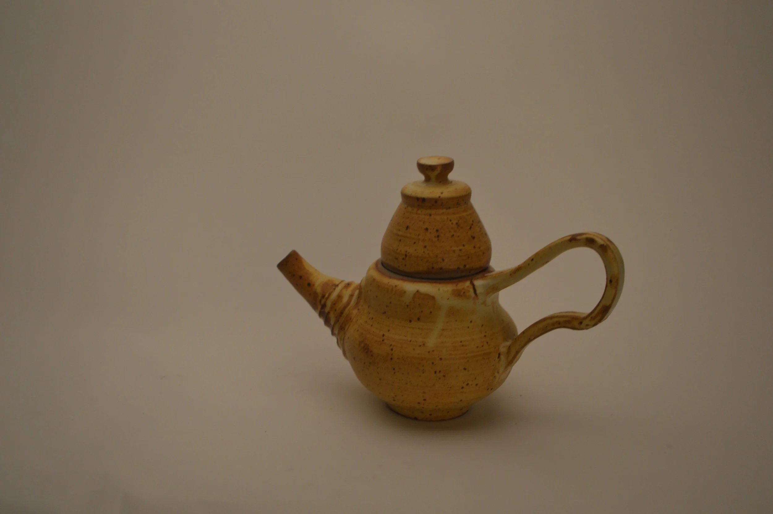 Ceramic teapot with a lid, spout, and curved handle, beige with dark speckles, placed against a plain background.