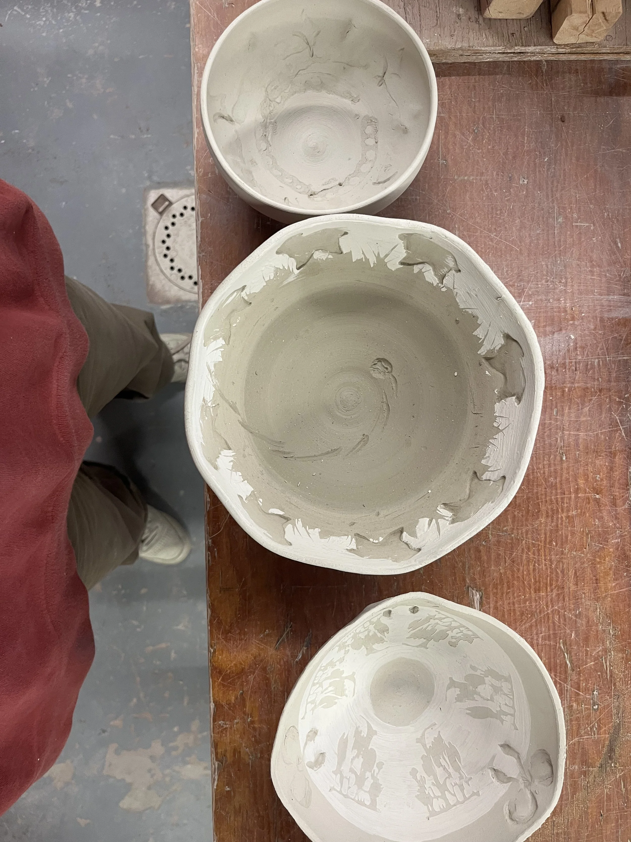 Three empty, unfinished clay bowls on a wooden work surface.