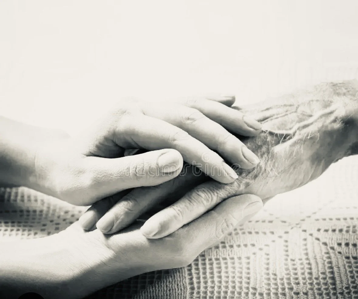 A younger hand gently holding the wrist of an older, wrinkled hand.