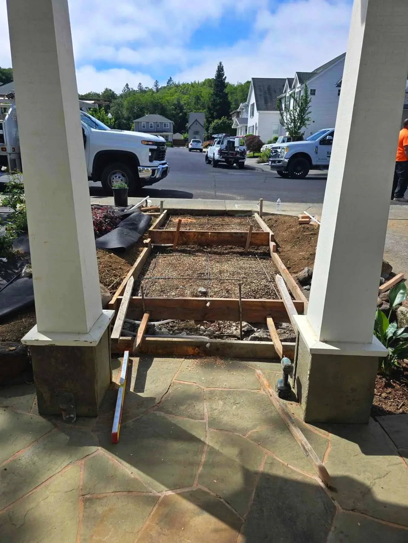 Pavered patio with two white wood columns. Steps mid construction leading to sidewalk.