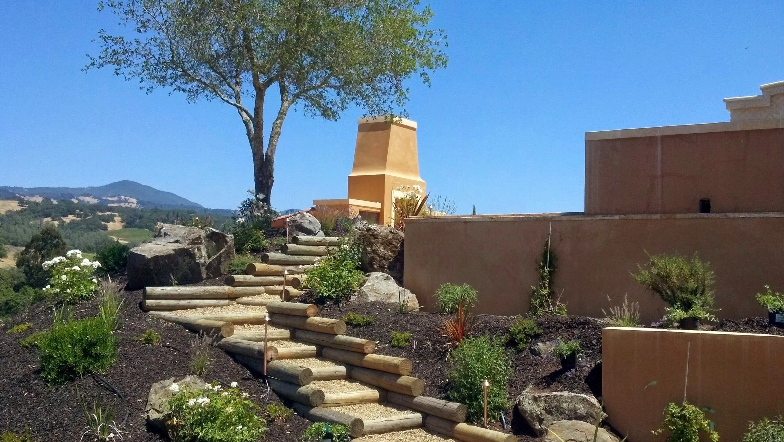 Stone steps placed in a small hill with retaining wall leading to a patio with outdoor fireplace