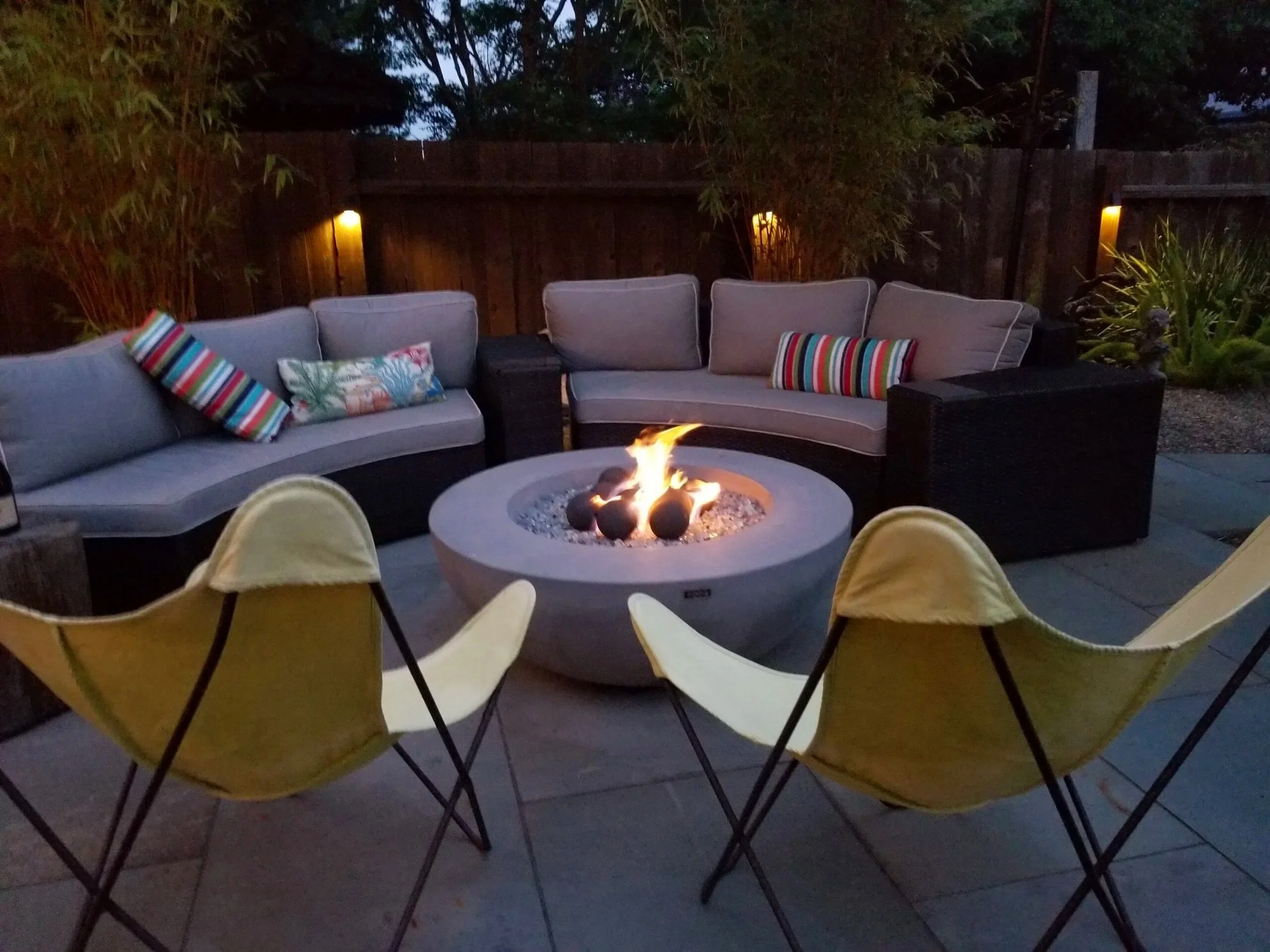 Bowl shaped Fire Pit on a pavered patio surrounded by plants and chairs