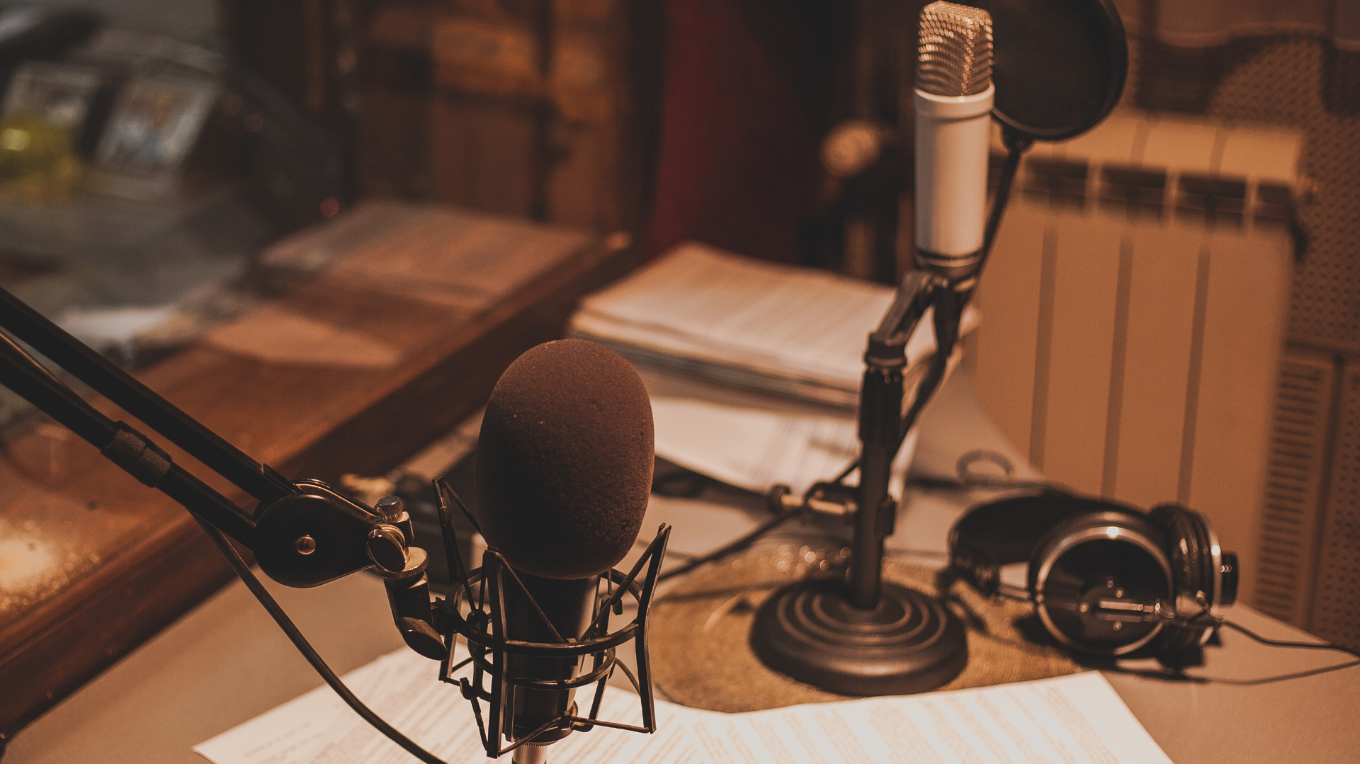 A radio station workspace with a microphone, headset, and paper files on a desk.