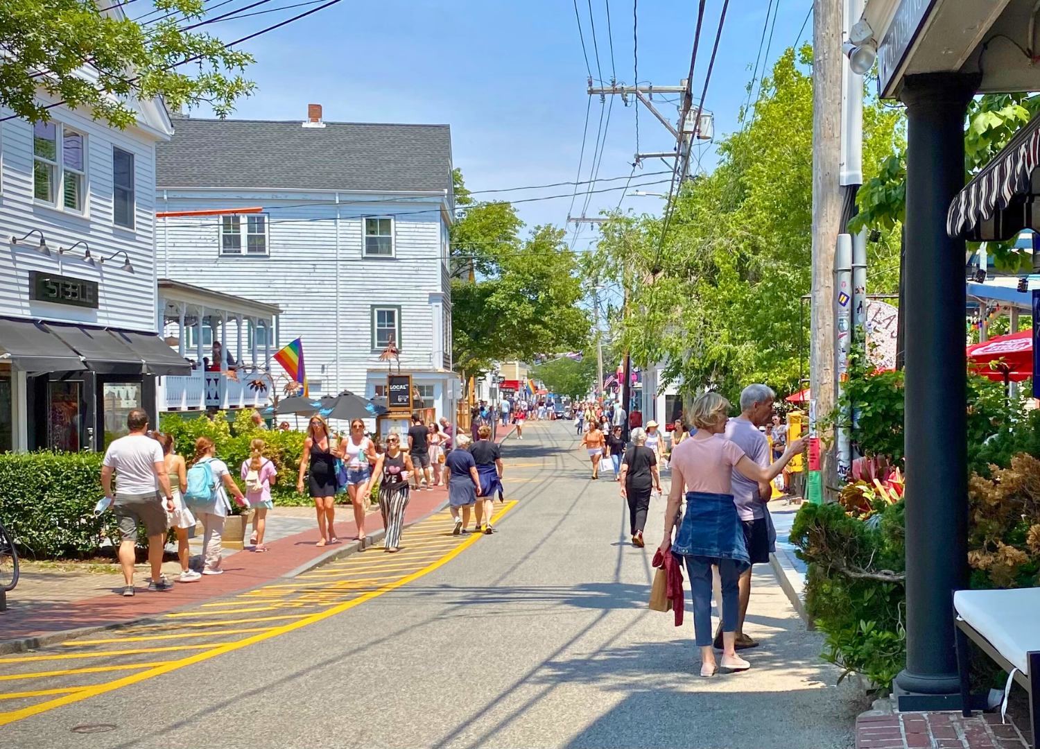 People enjoying a sunny day on a Cape Cod street, capturing the charm of local life and tourism.
