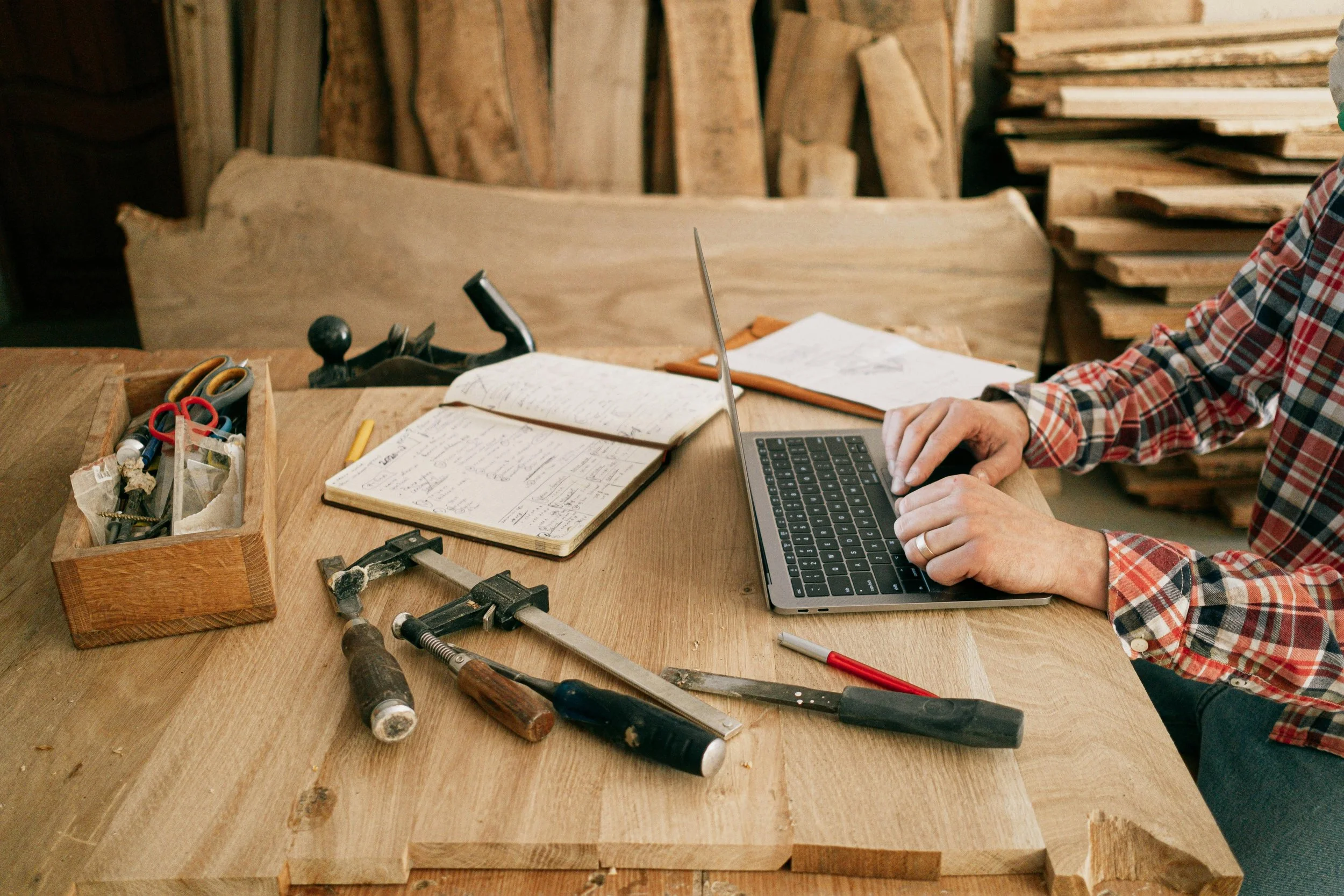 Local business owner using computer at a workshop desk with different tools and notebook.