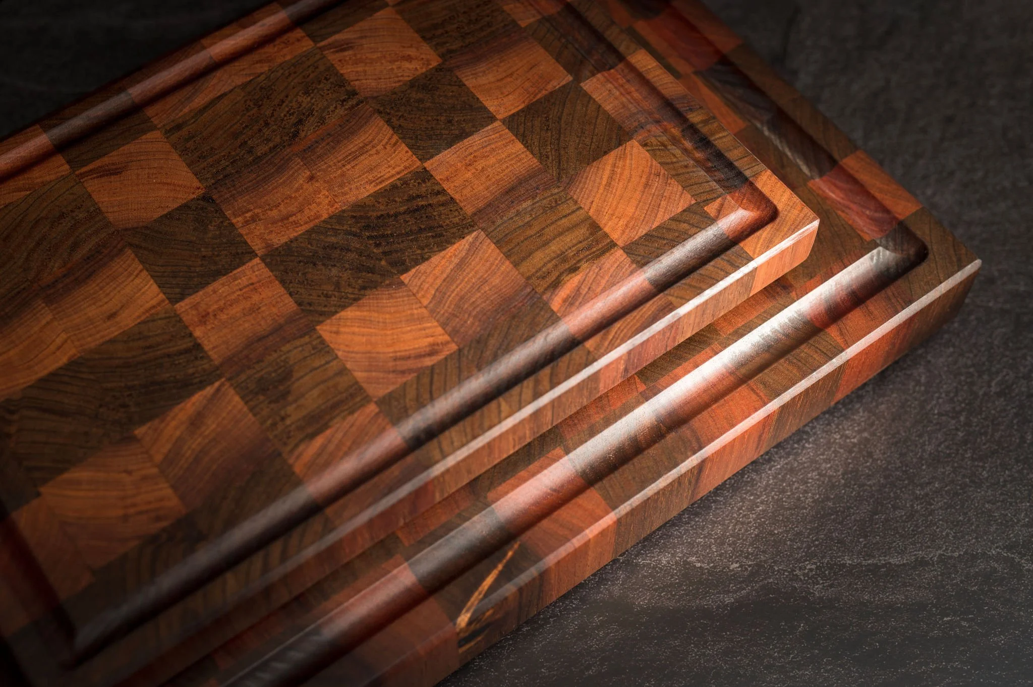 Close-up of a wooden chessboard with alternating dark and light wood squares, placed on a dark surface.