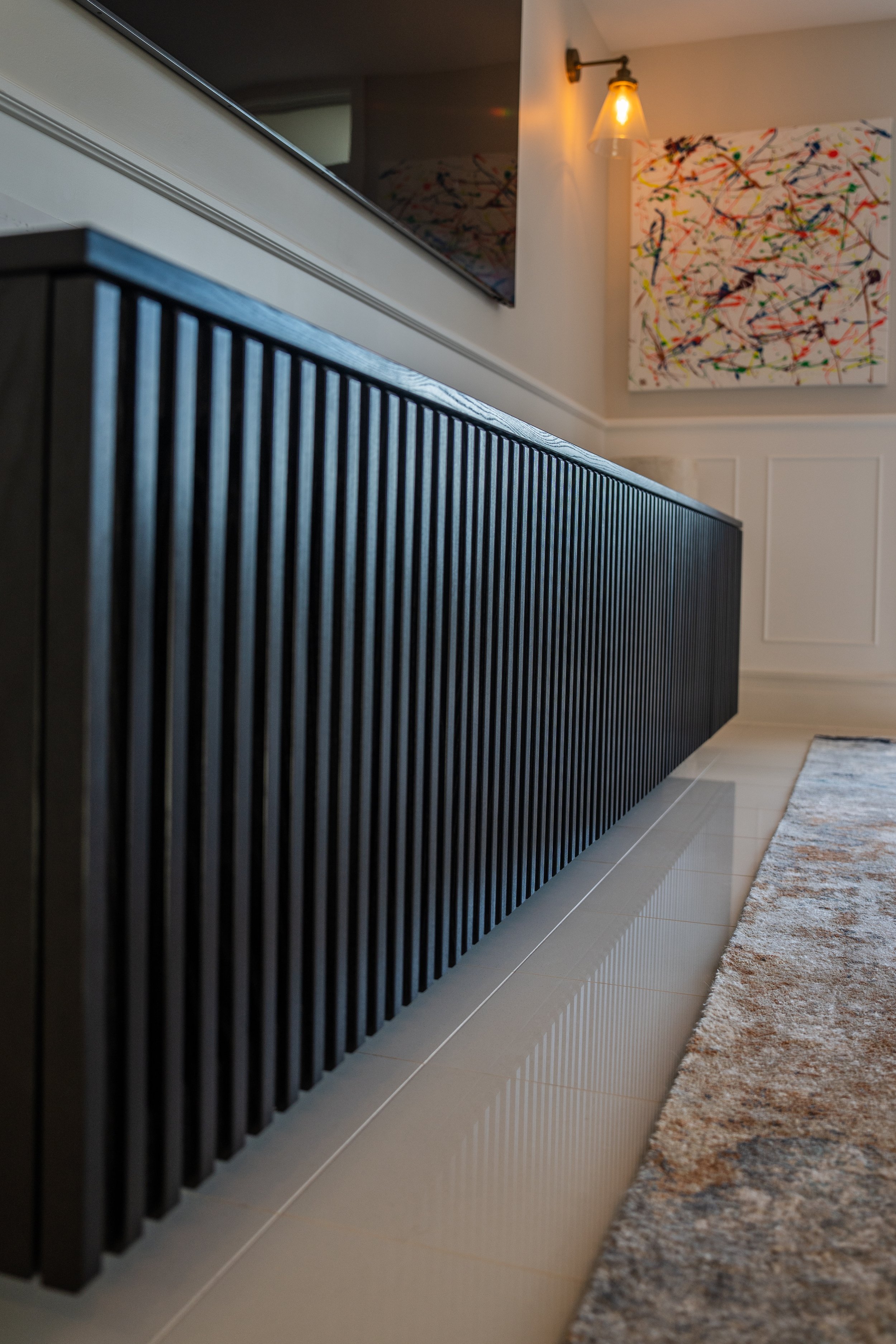 Close-up of a black wooden cabinet with vertical slats, located in a modern living room with a wall-mounted TV, colorful abstract artwork, and a wall sconce