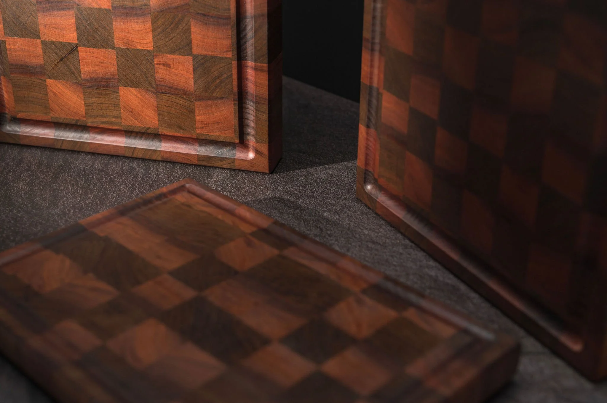 Close-up of three wooden chessboards with checkered patterns, positioned on a dark textured surface.