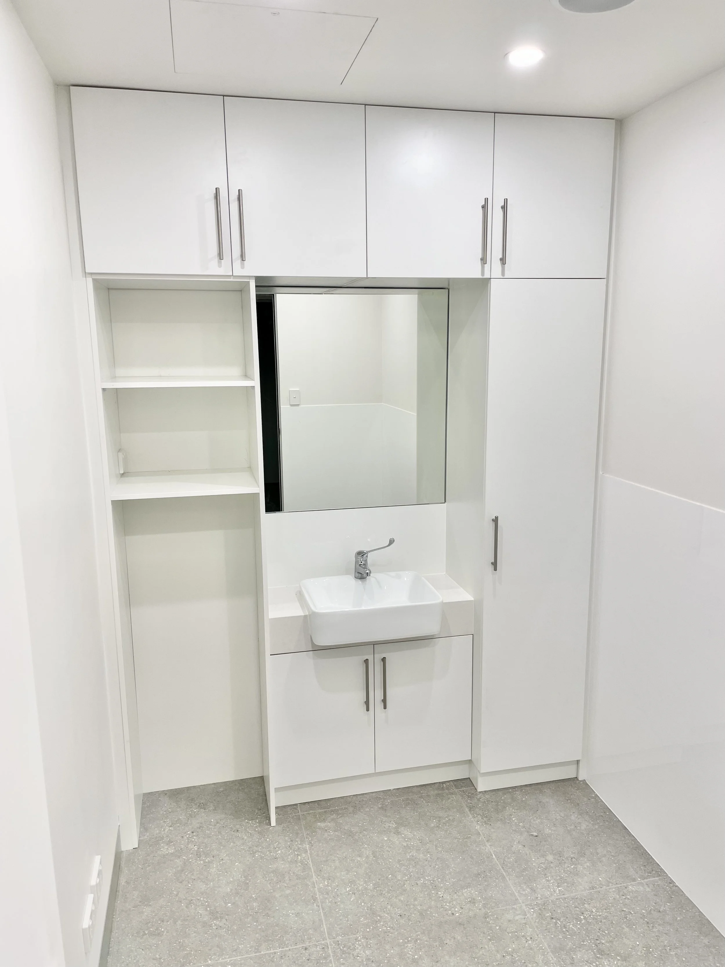 White bathroom with a sink, mirror, and storage cabinets.