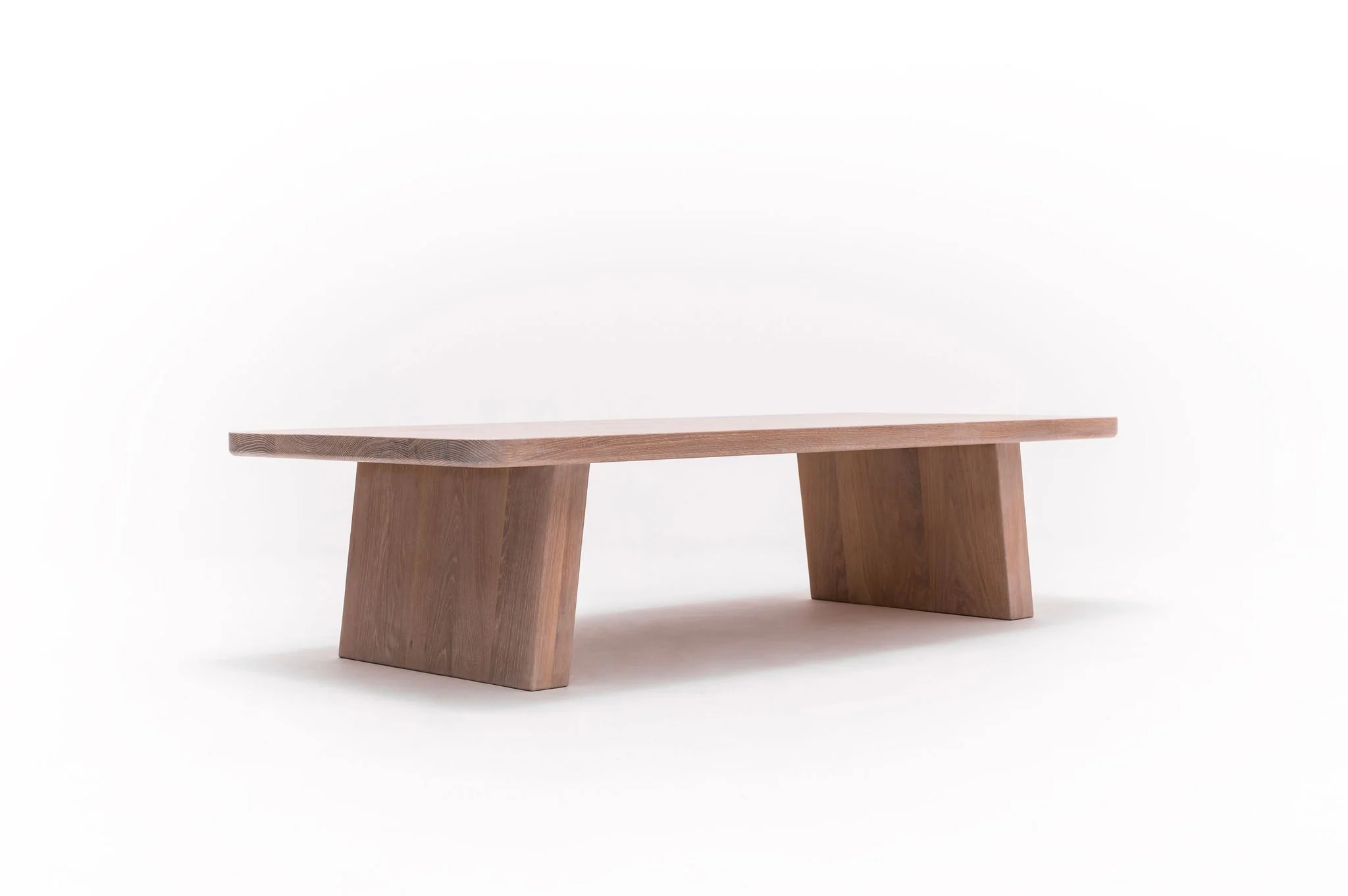 A minimalist, modern wooden bench with a flat top and two angled supports, set against a plain white background.