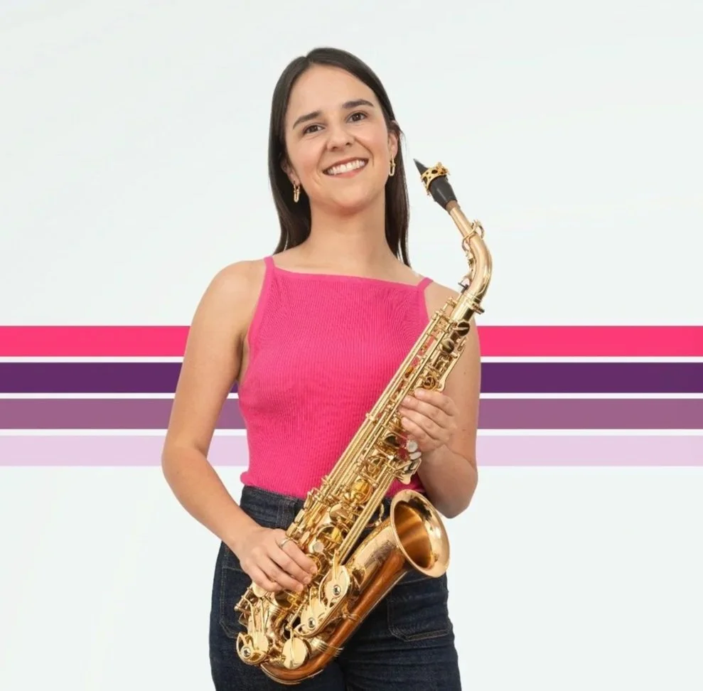A young woman with long dark hair and a pink sleeveless top holding a gold saxophone, smiling at the camera against a white background with pink and purple horizontal stripes.