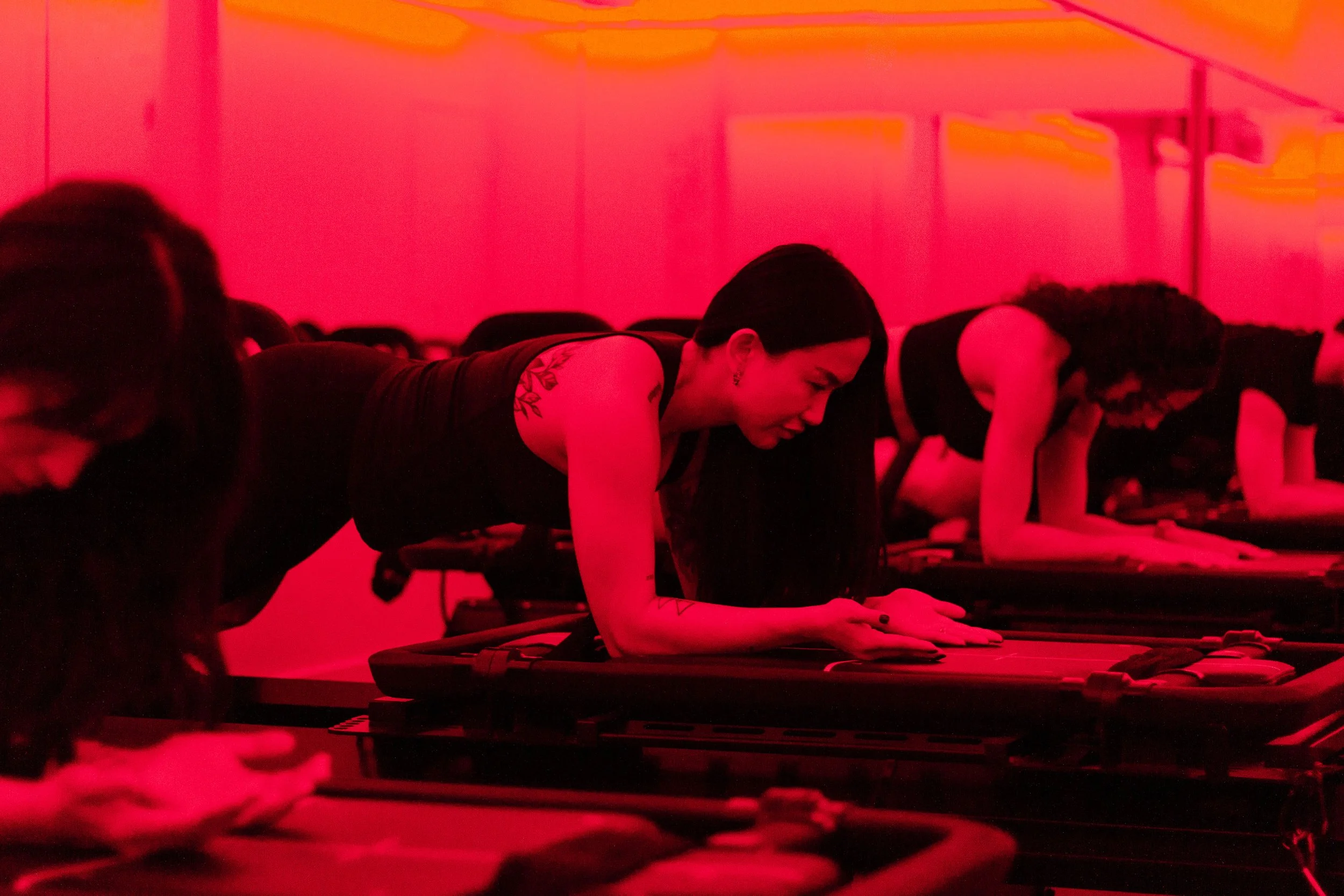 People doing yoga or group exercise on mats in a dimly lit room illuminated with red lighting.