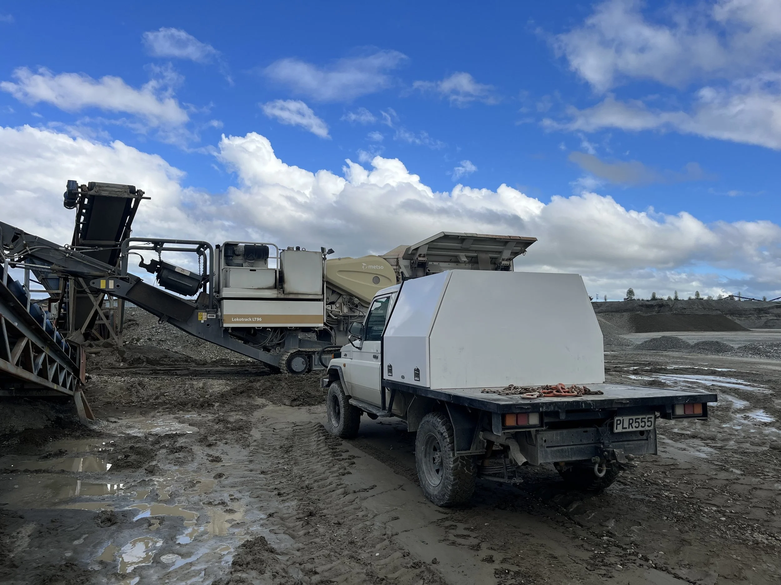 Construction vehicles and equipment on a muddy construction site under a partly cloudy sky.