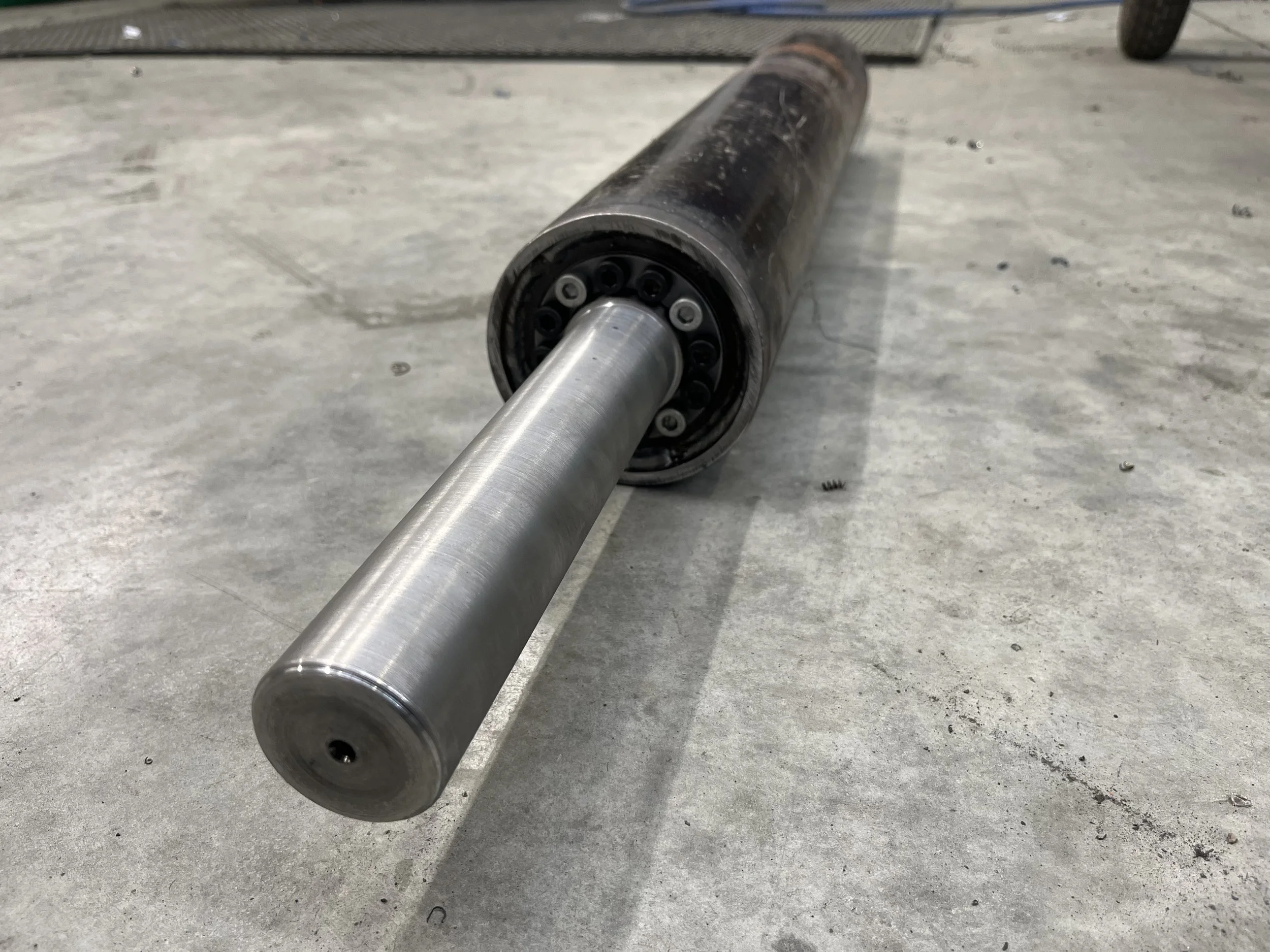 A large metal roller or cylindrical object lying on a concrete floor.