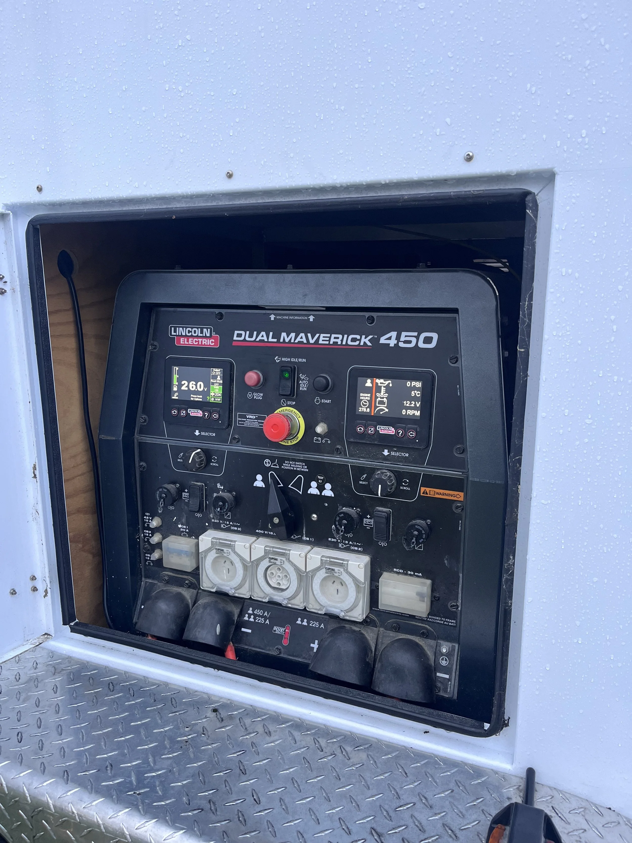 Close-up of a Lincoln Electric Dual Maverick 450 welding machine installed in a weatherproof enclosure, with control panel and power outlets visible.