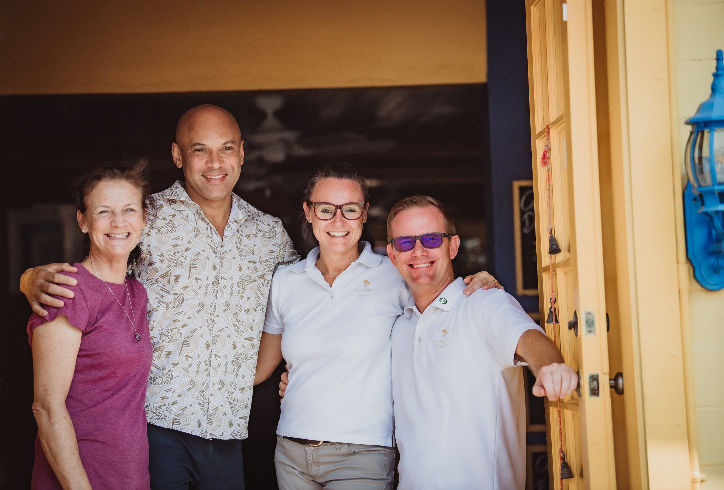 Four people, two women and two men, standing together and smiling, in a restaurant or cafe setting.