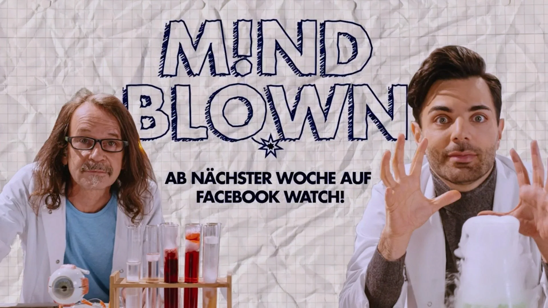 Two men dressed as scientists with laboratory equipment in front of a crumpled paper background with the text 'MIND BLOWN' and German text indicating a Facebook Watch debut.