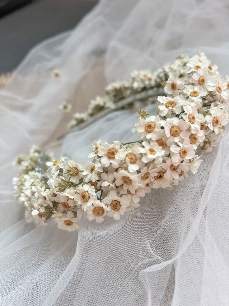 A white floral headband or crown made of small white and peach-colored flowers resting on white tulle fabric.