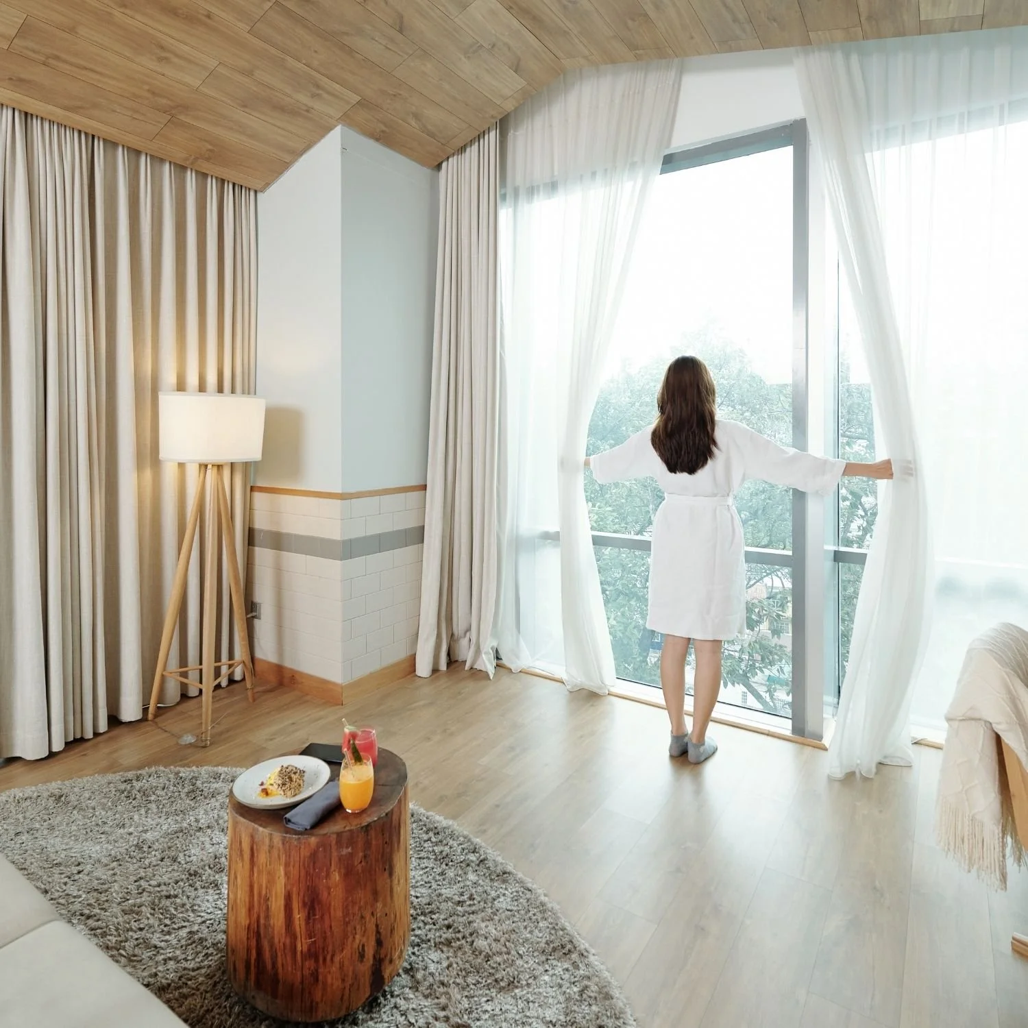 Woman opens custom-made sheer curtains in a bright room, representing Brighton Alterations’ soft furnishings and tailored window treatments.